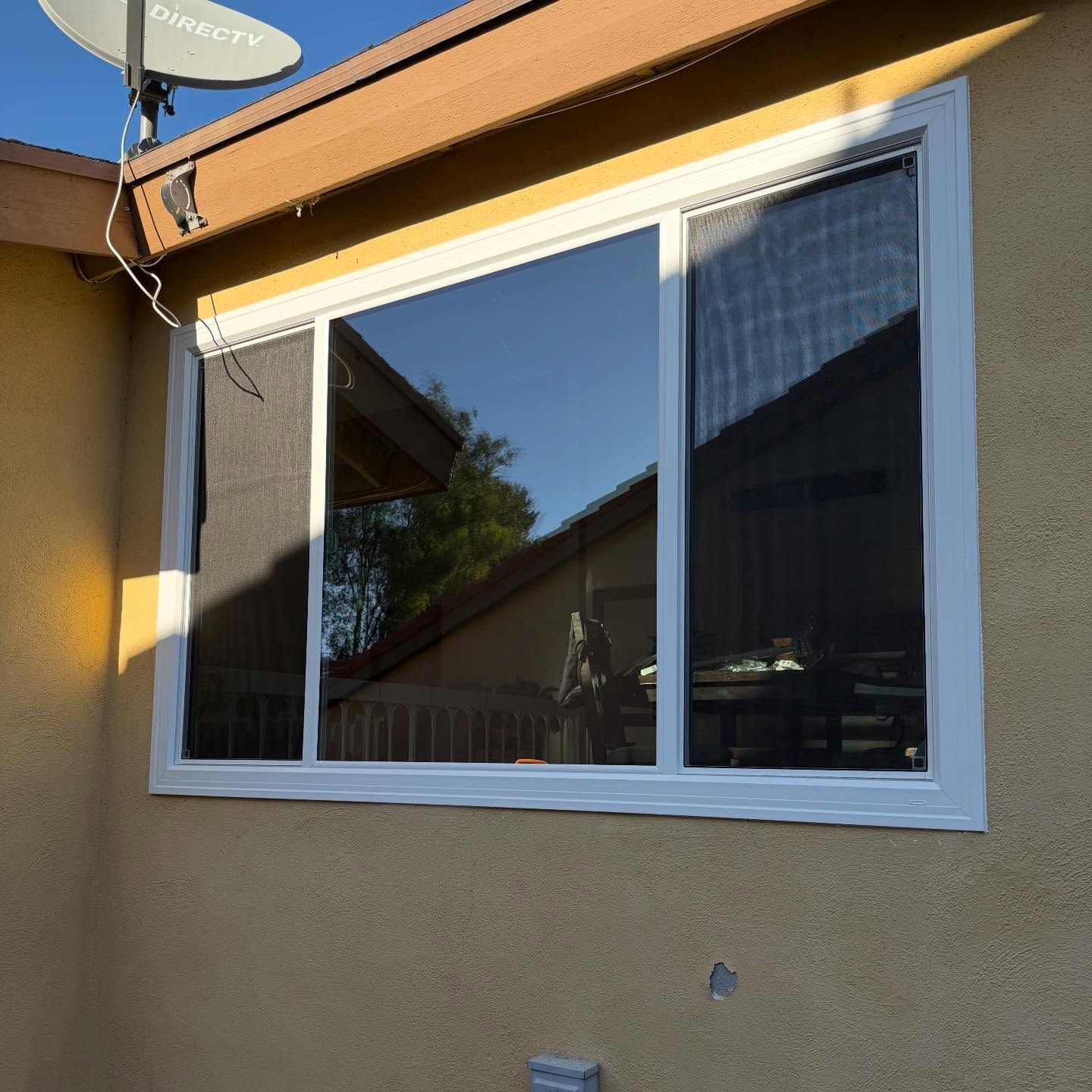 Residential house exterior with a large white-framed window and tan stucco wall in sunlight