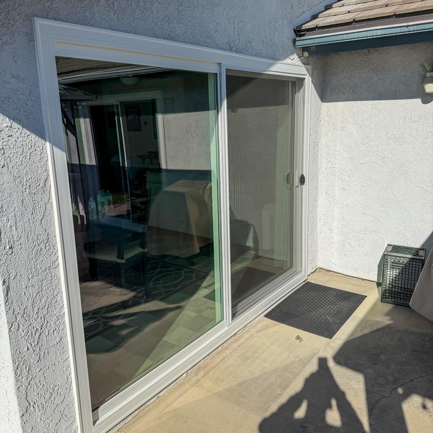 Sunny patio with open sliding glass door leading into a room with curtains and a small mat outside