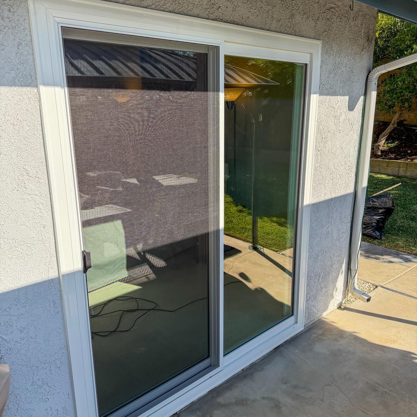 Sliding glass door with white frame beside a patio, reflecting sunlight.