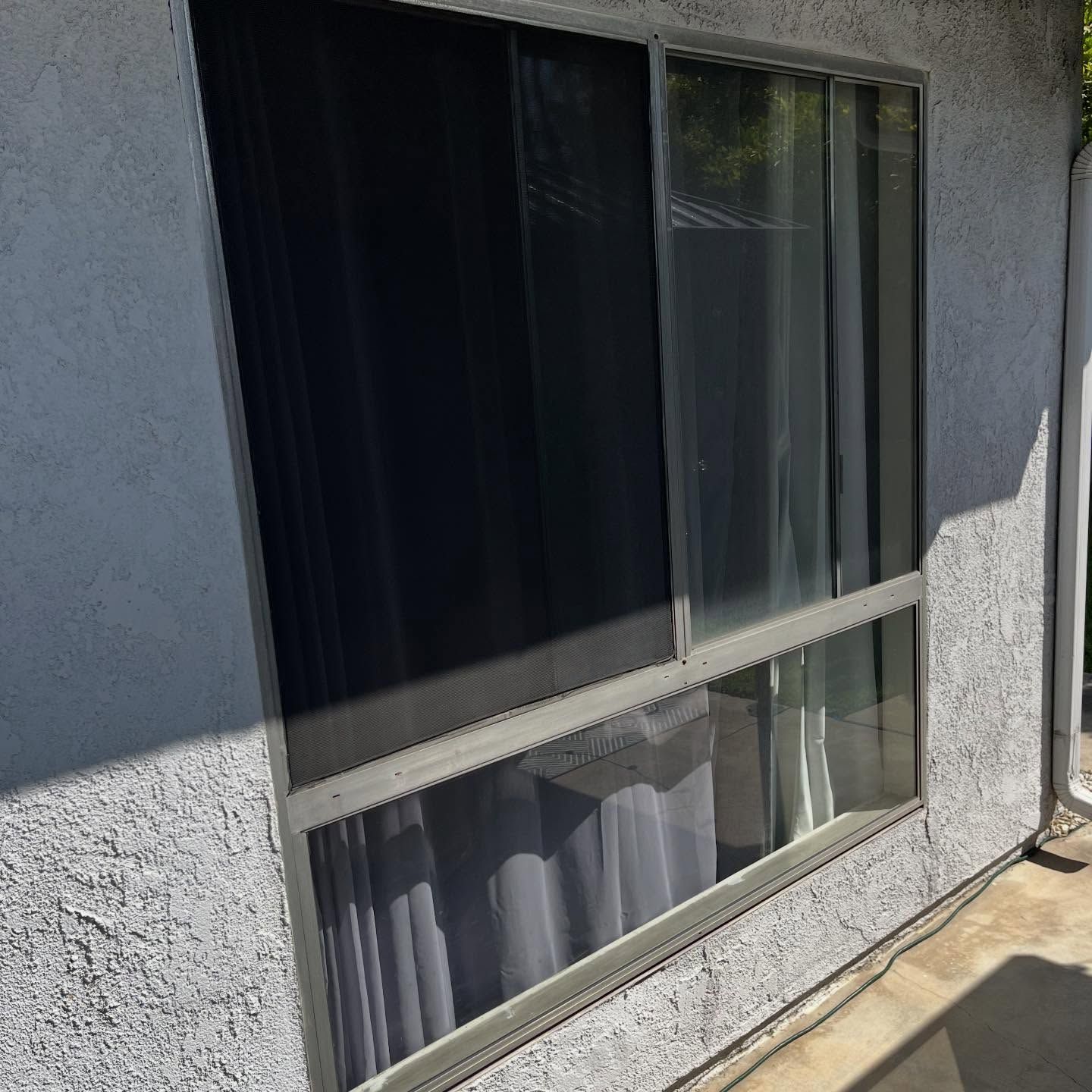 Sliding glass window with curtains on a stucco exterior wall in sunlight