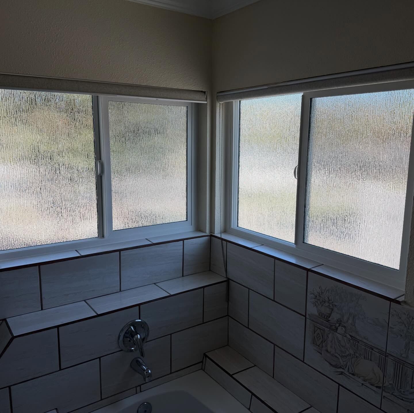 Small tiled bathroom corner with frosted windows and a sink below.