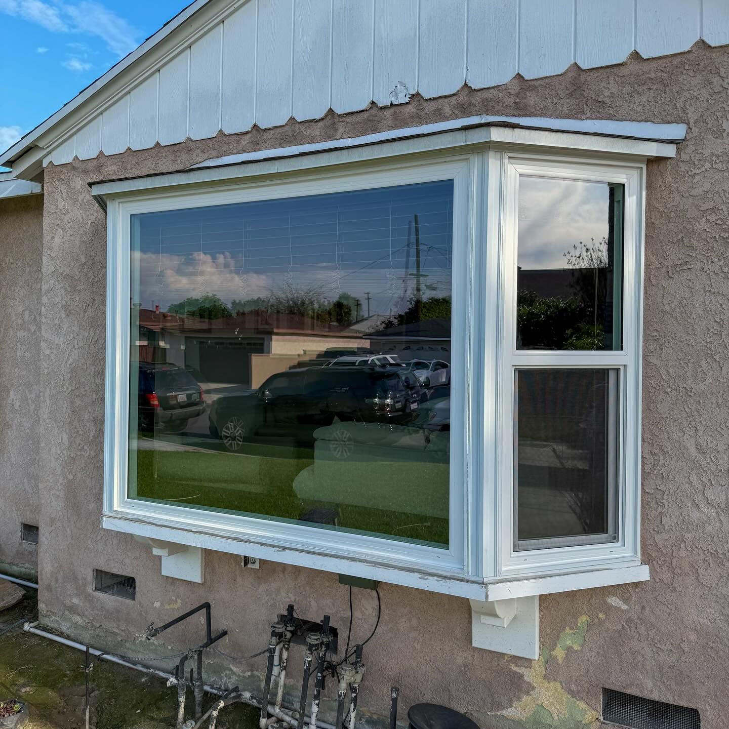 White bay window on beige stucco house, reflecting cars and sky.