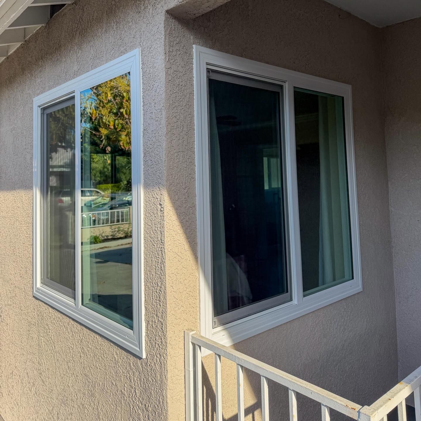 Corner of a beige stucco building with white-framed windows and a balcony railing