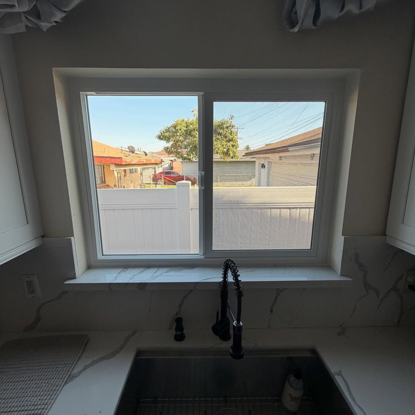 Kitchen sink beneath a window, showing a suburban street and garage outside.