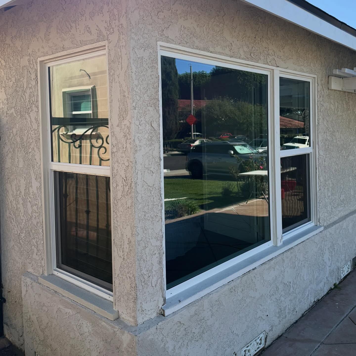 Stucco house corner with two white-framed windows and a reflective sliding glass window.