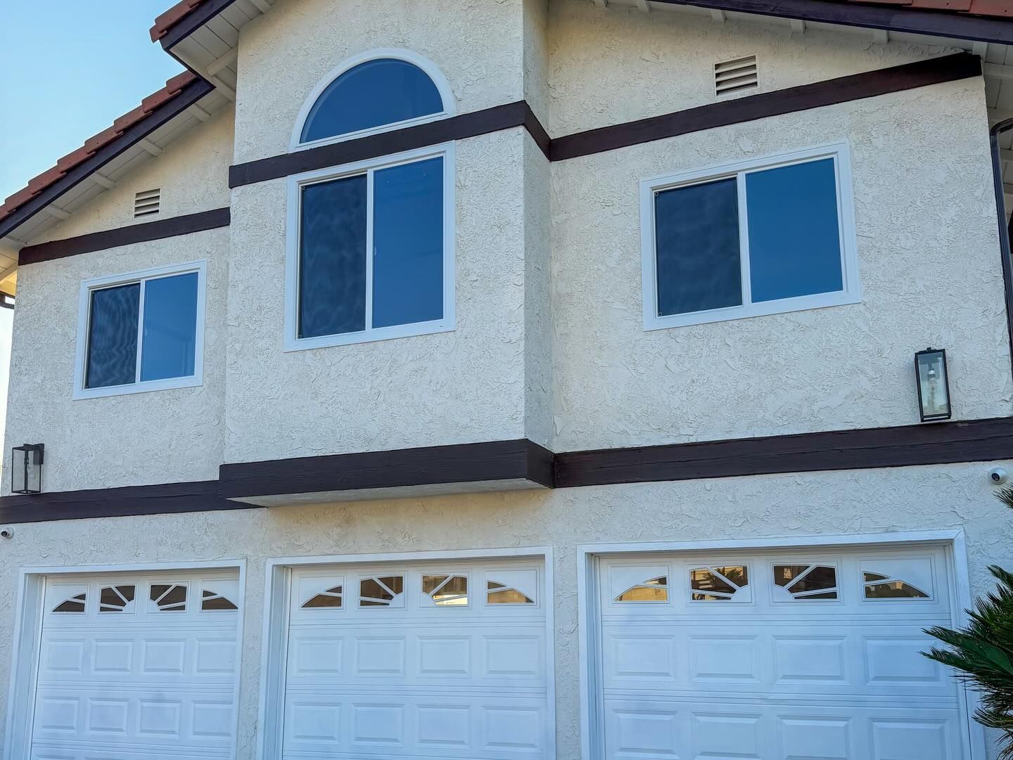Two-story house with white stucco exterior, blue windows, brown trim, and three garage doors