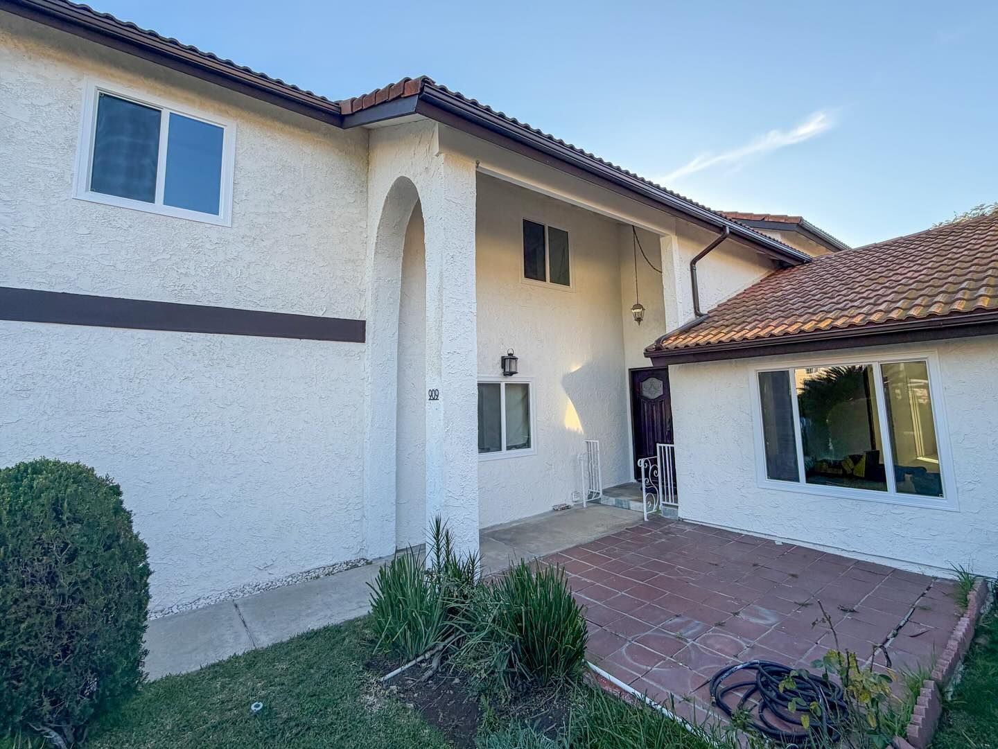 Stucco house courtyard with arched entry, tiled roof, and brick patio under a clear blue sky