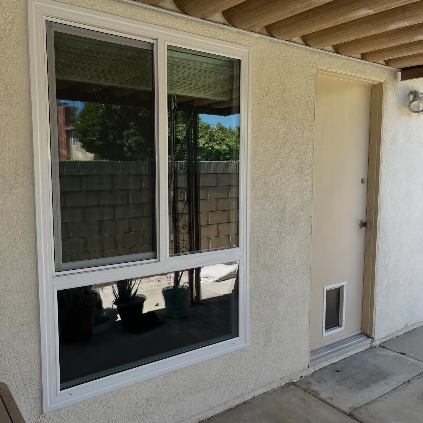 White stucco exterior wall with a large window and a door beside a small vent panel.