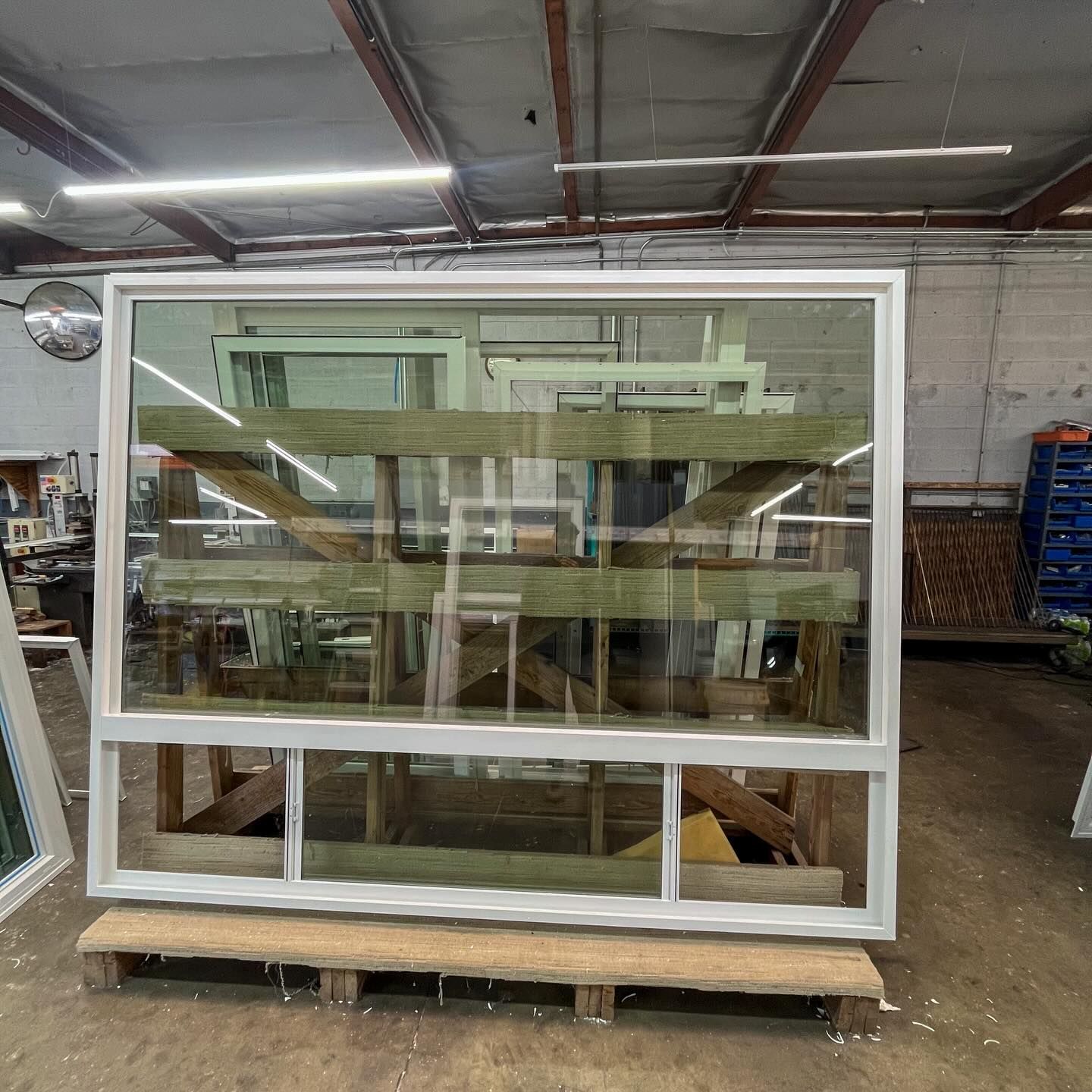 Large white-framed glass window unit on a wooden pallet in an industrial warehouse.