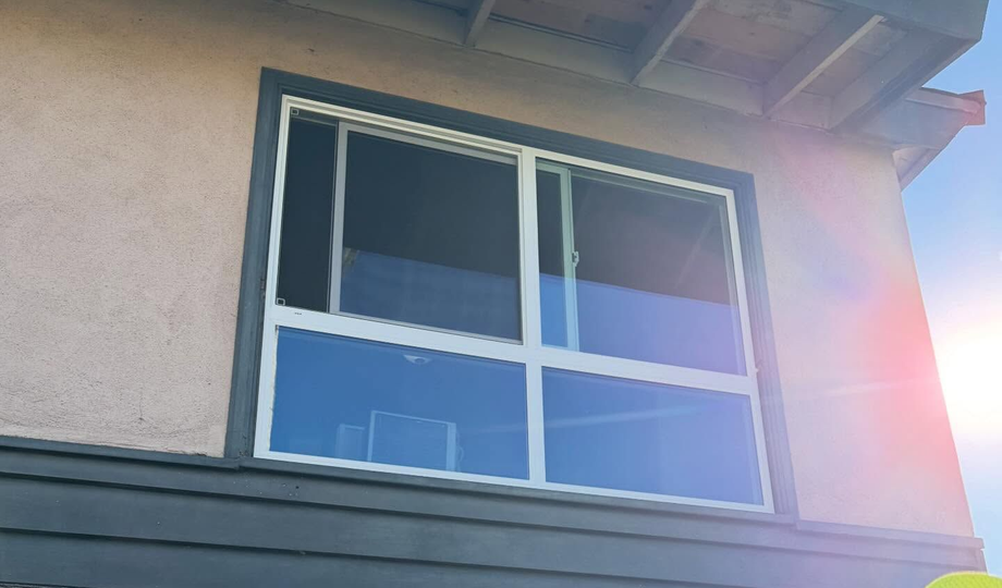 Sunlit exterior window with white trim on a stucco building under the eaves