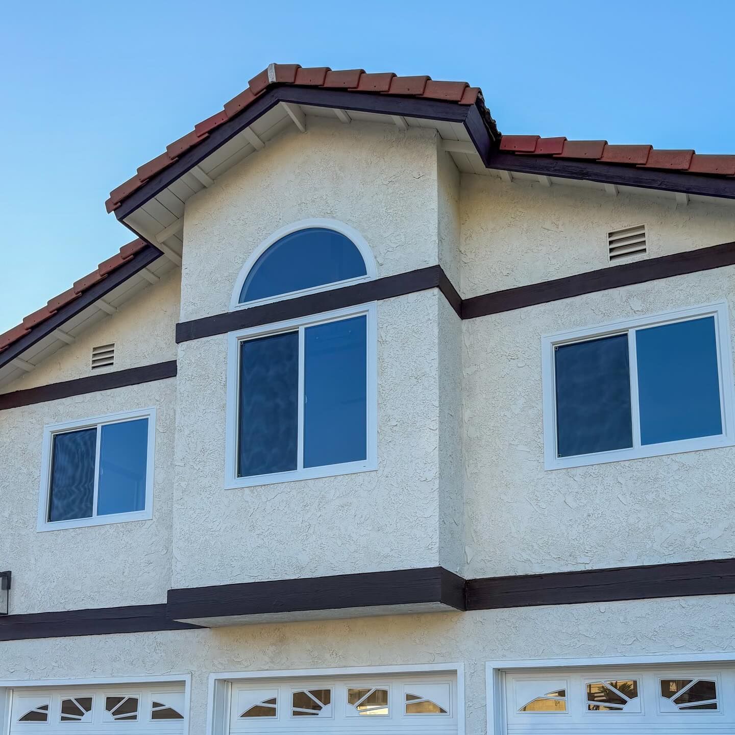 Exterior of a white stucco house with brown trim, red roof tiles, and garage doors below