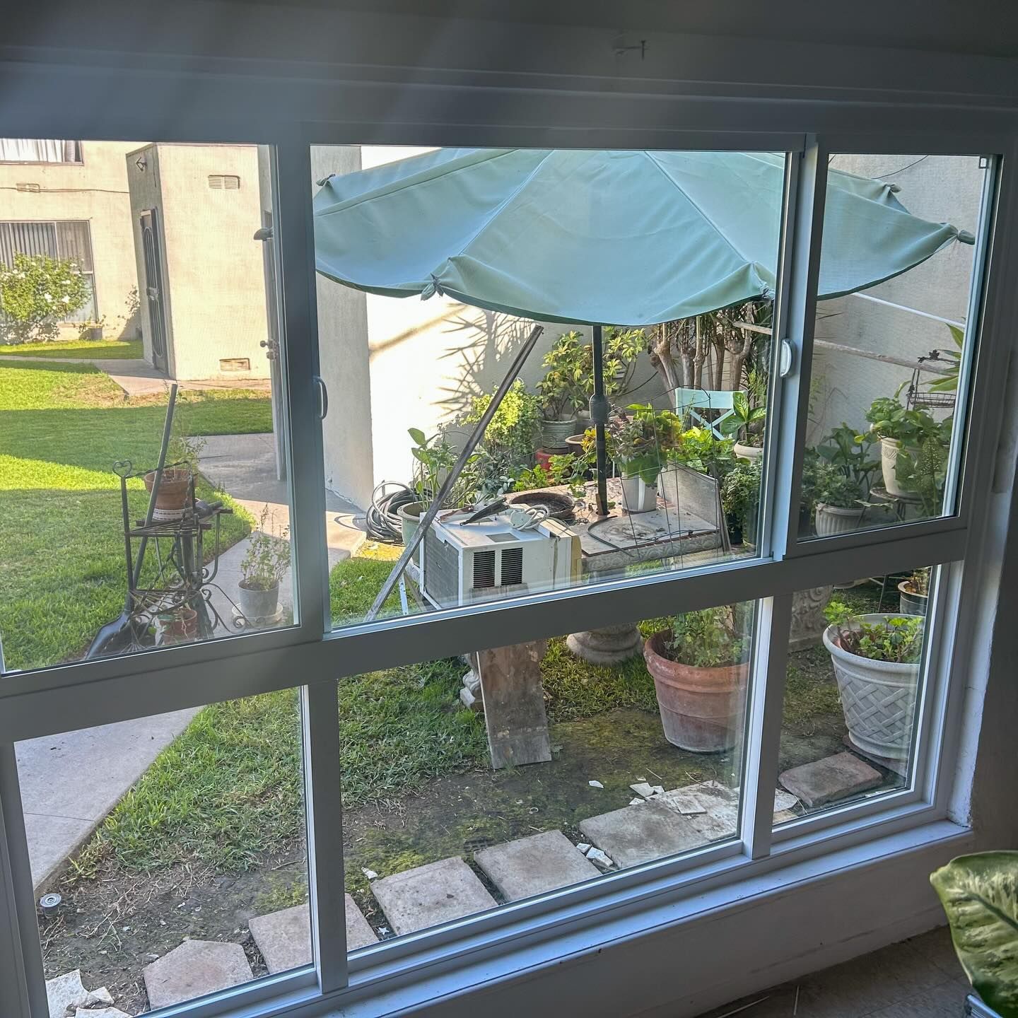 View through a window of a small patio garden with potted plants, a white umbrella, and outdoor seating