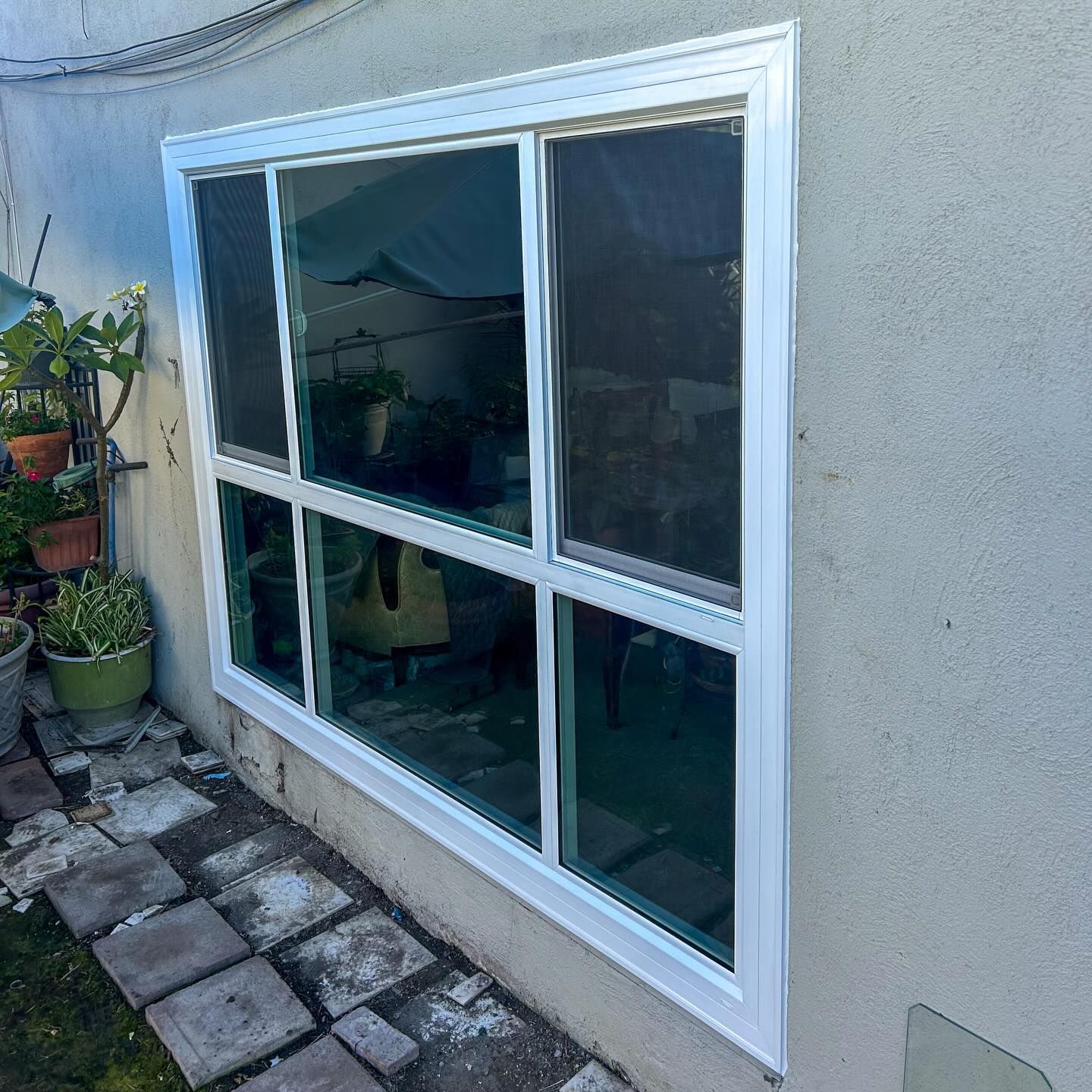 White-framed window on a stucco exterior wall beside a stone patio and potted plants