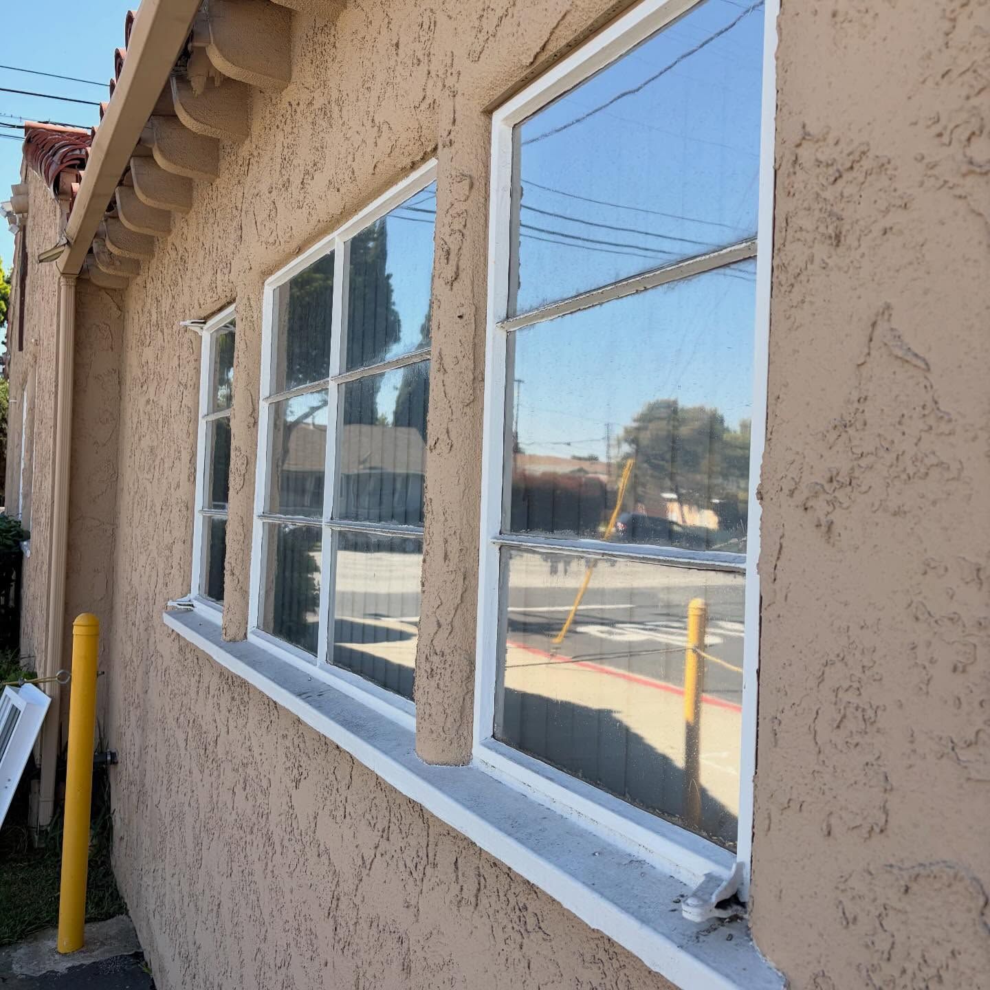 Stucco exterior wall with white-framed windows reflecting a street scene, beside a yellow post.