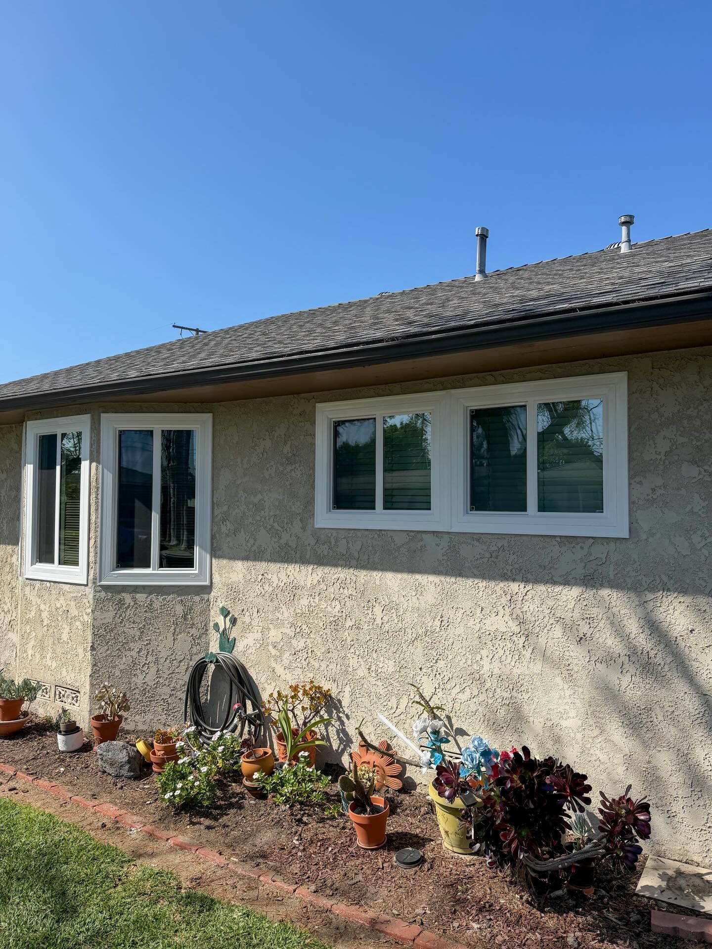 Single-story house exterior with gray siding, white-trimmed windows, and flower pots along the wall