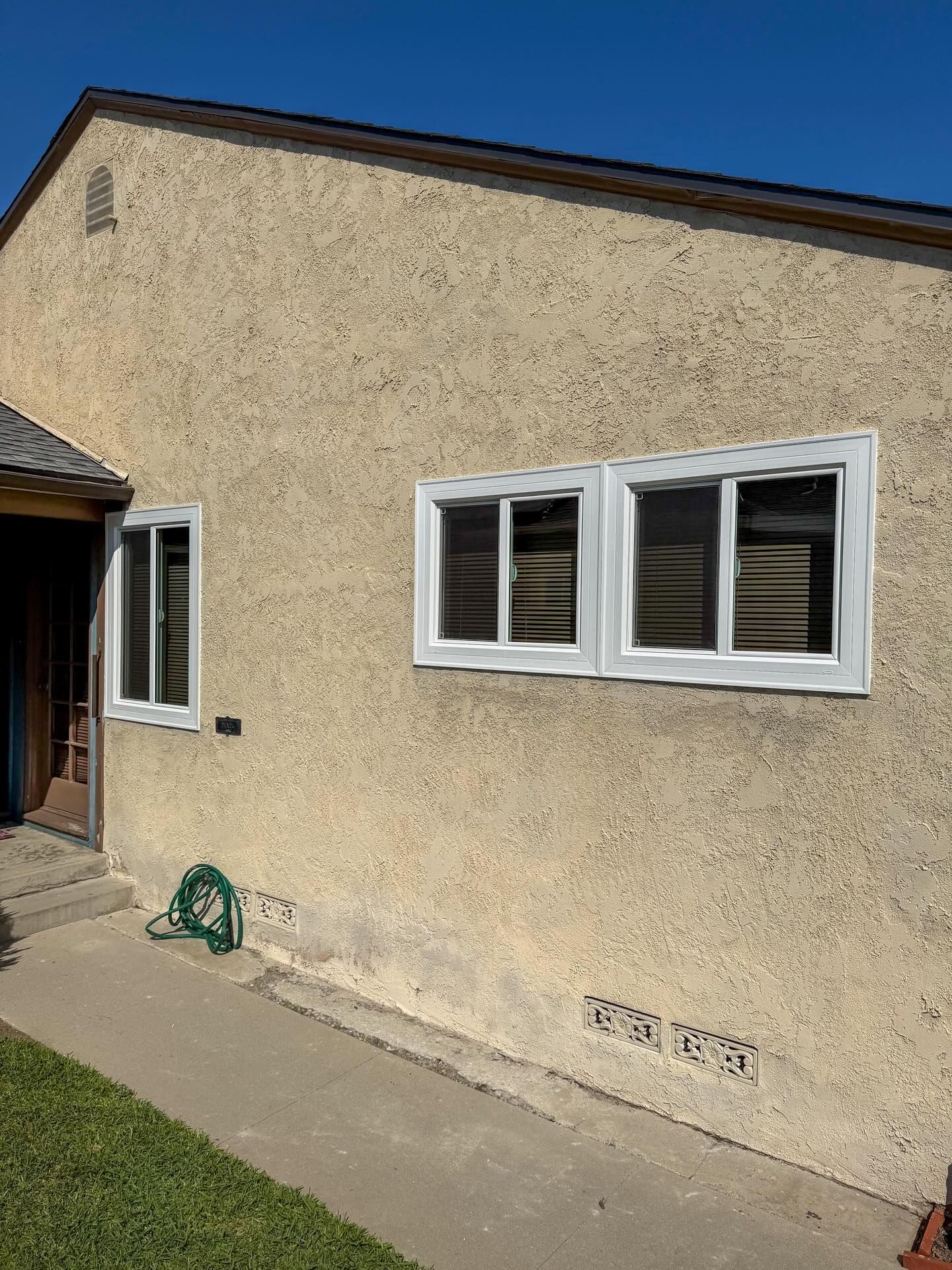 Exterior stucco wall with two white-framed windows and a small side entrance under a blue sky