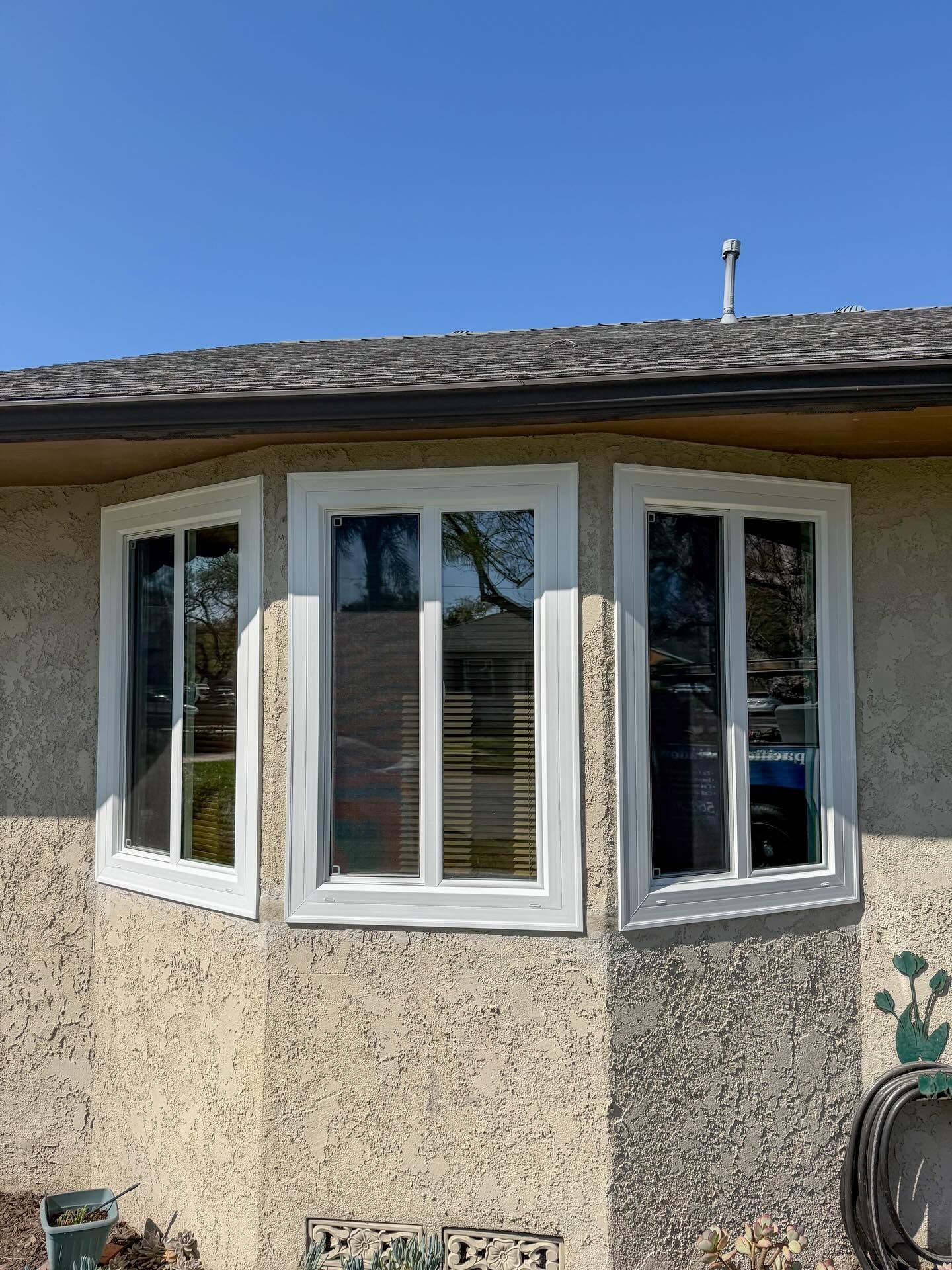 Exterior corner of a beige house with white bay windows under a blue sky