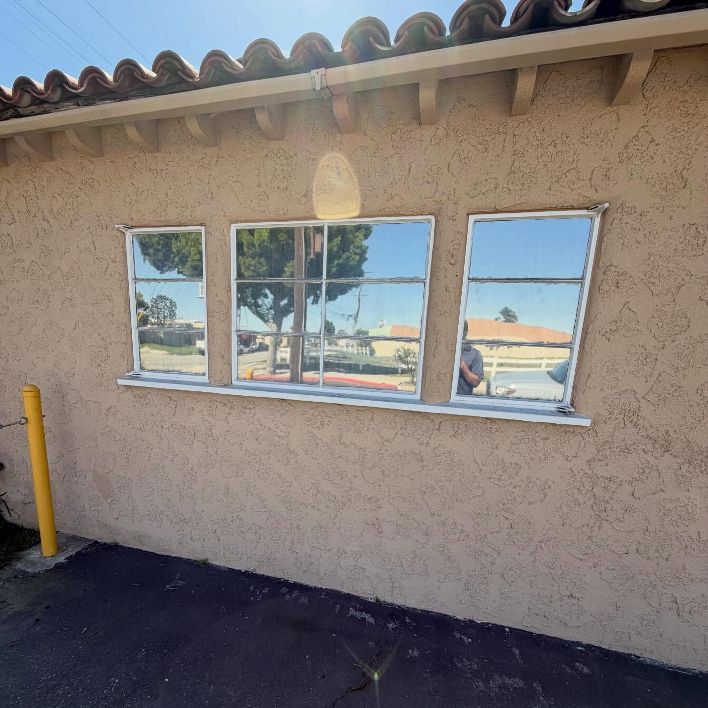 Stucco building wall with three windows, reflecting an outdoor parking lot under a tiled roof.
