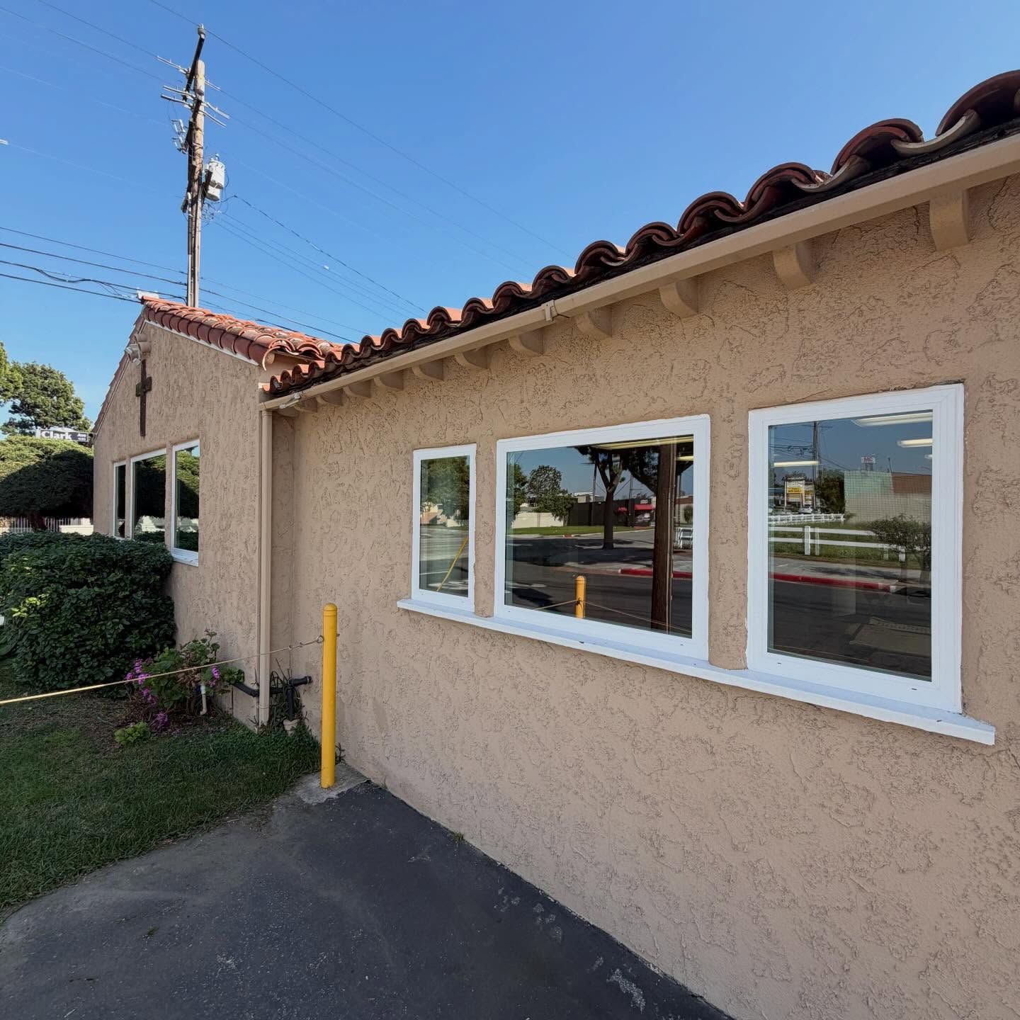 Stucco building exterior with white-framed windows, red tile roof, and a paved walkway under a blue sky