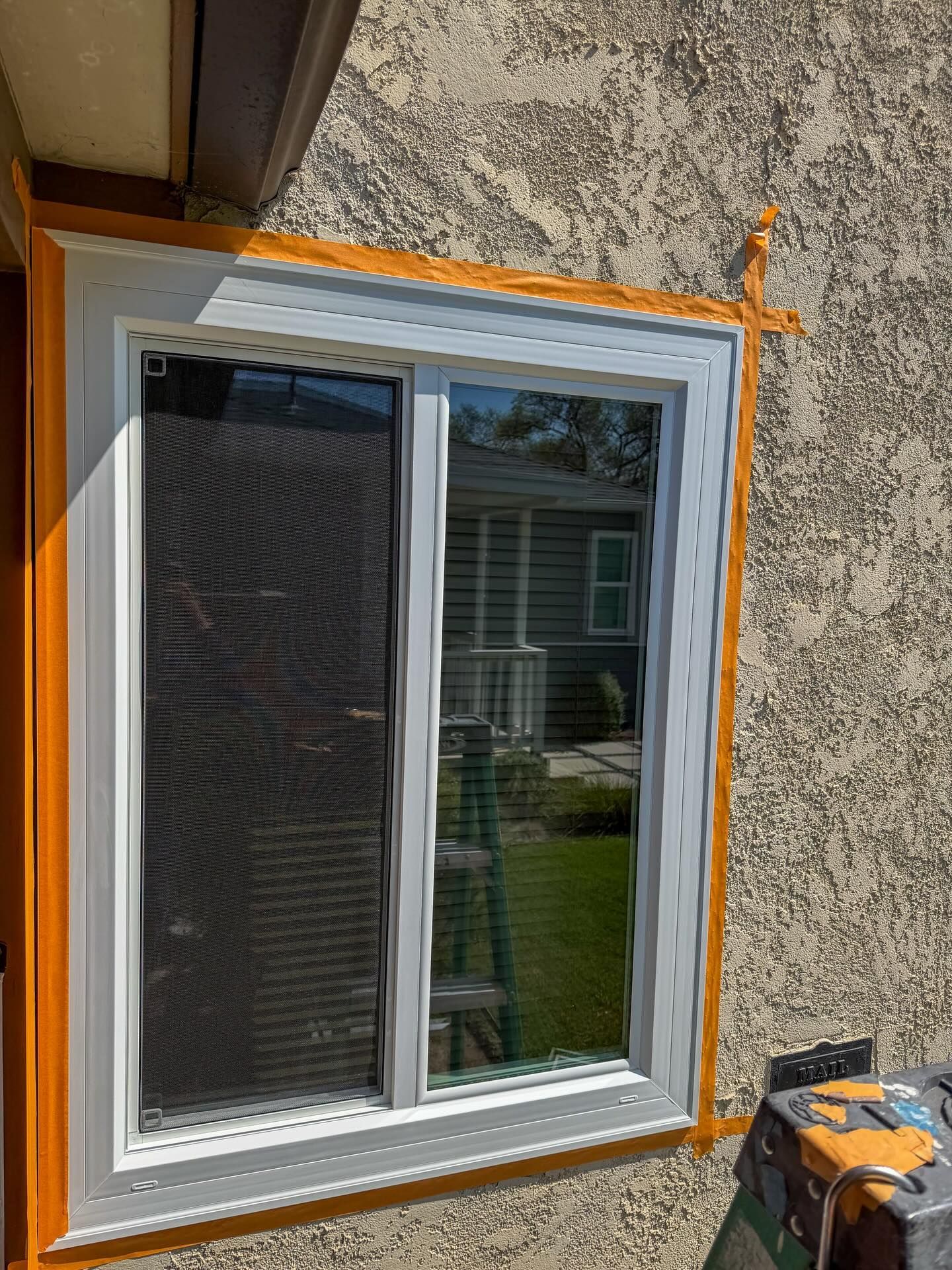 White-framed window set in rough stucco wall with orange spray paint marking around the trim.