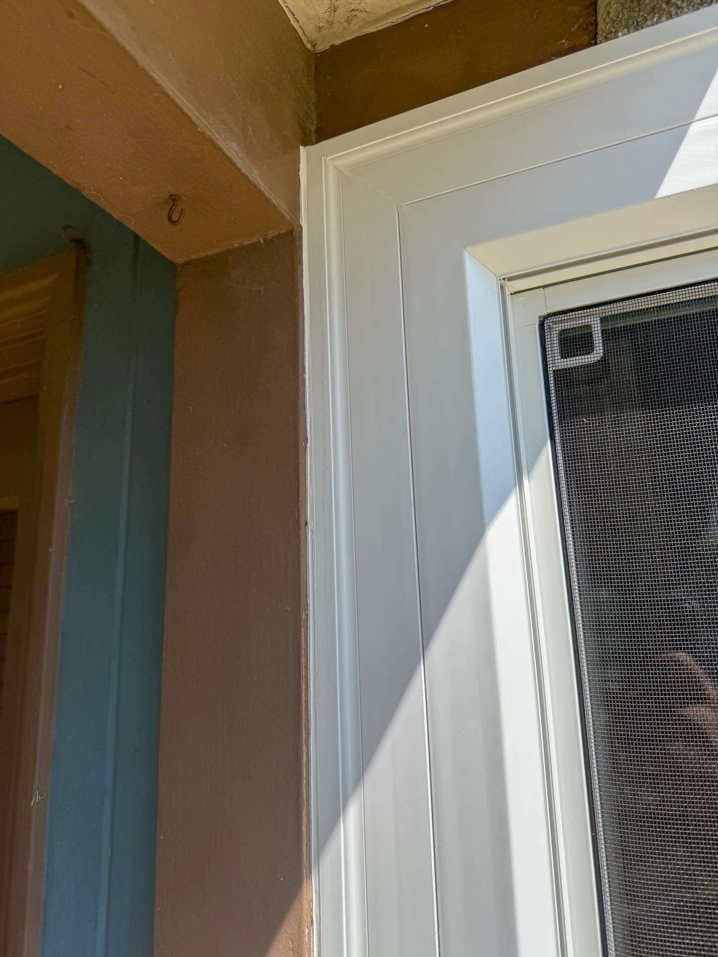 Close-up of a white front door frame beside a tan wall, with a screen door partially visible.
