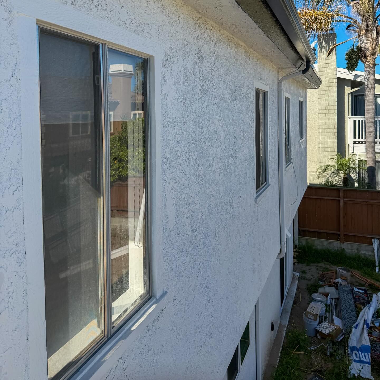 White stucco house exterior with sliding glass doors and narrow windows beside a fenced yard.