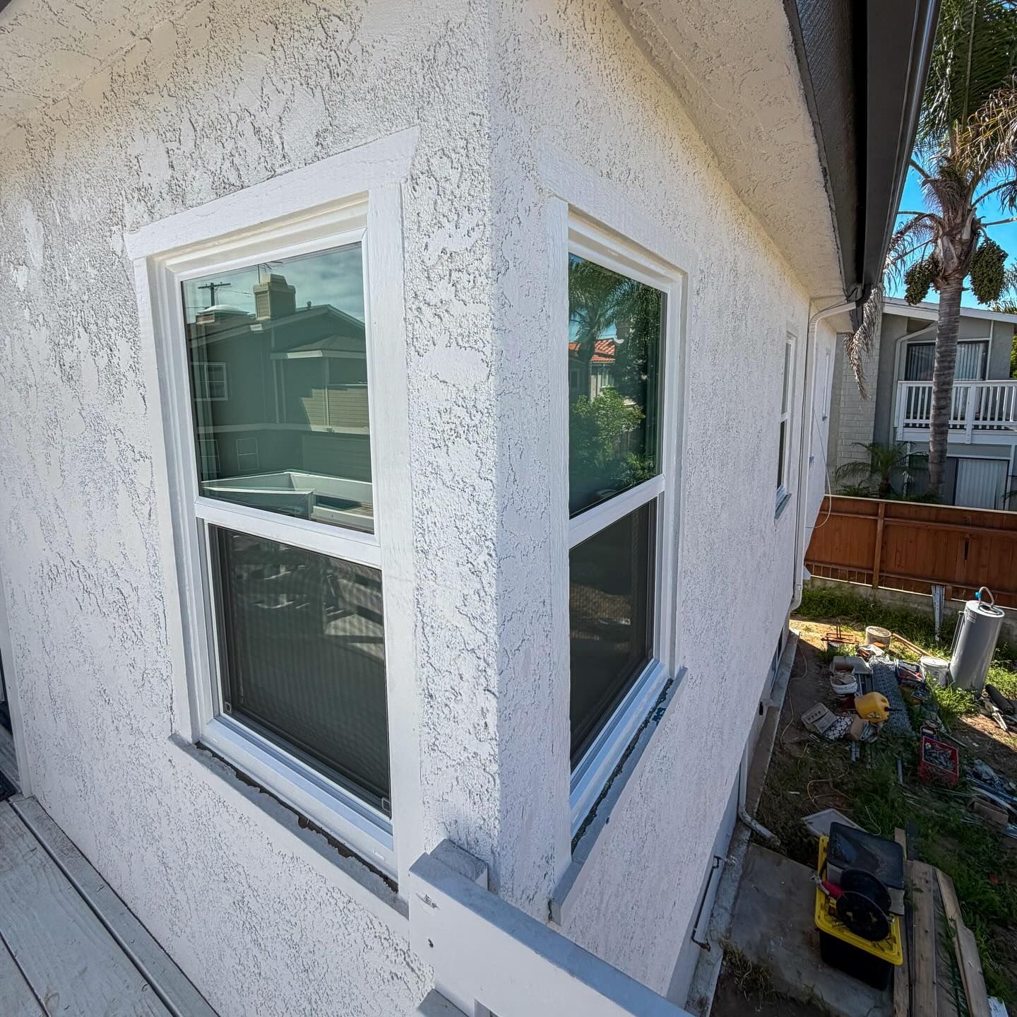 Corner view of a white stucco house exterior with two windows and a small yard below