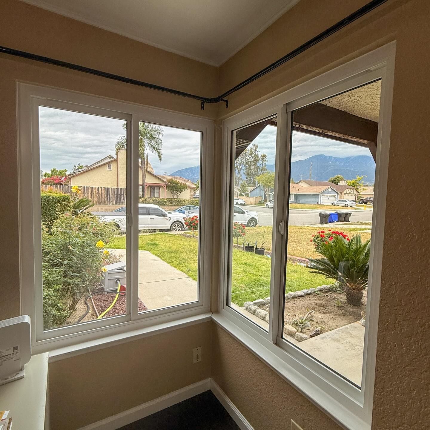 Corner window view of a suburban street, lawn, and neighboring houses from inside a room