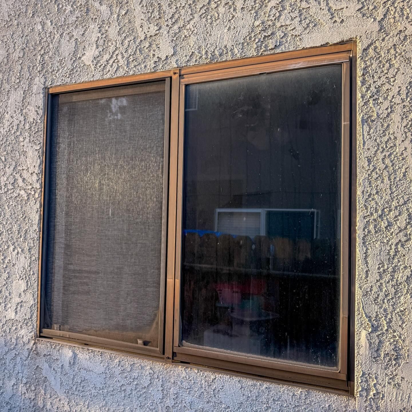 Two-pane window with dark glass in a tan stucco wall outdoors