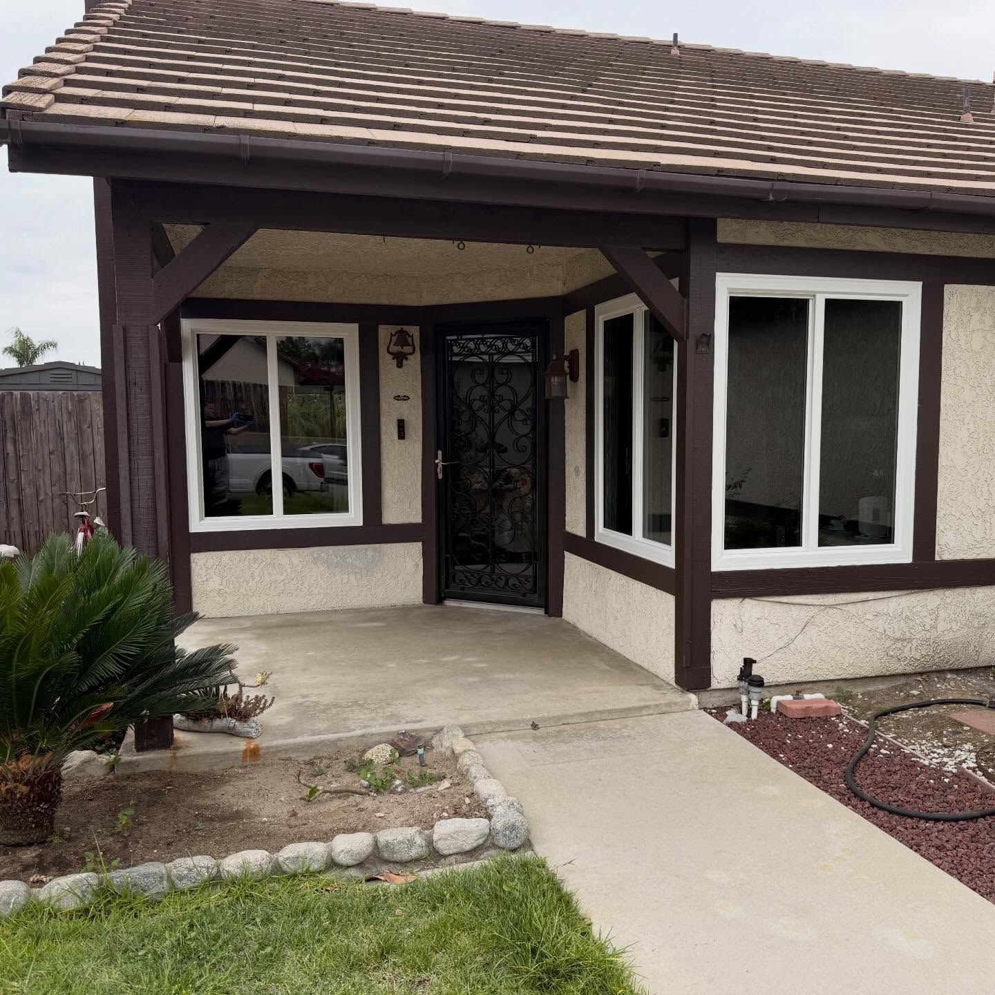 Front entrance of a beige stucco house with dark brown trim, arched porch, and decorative black security door.