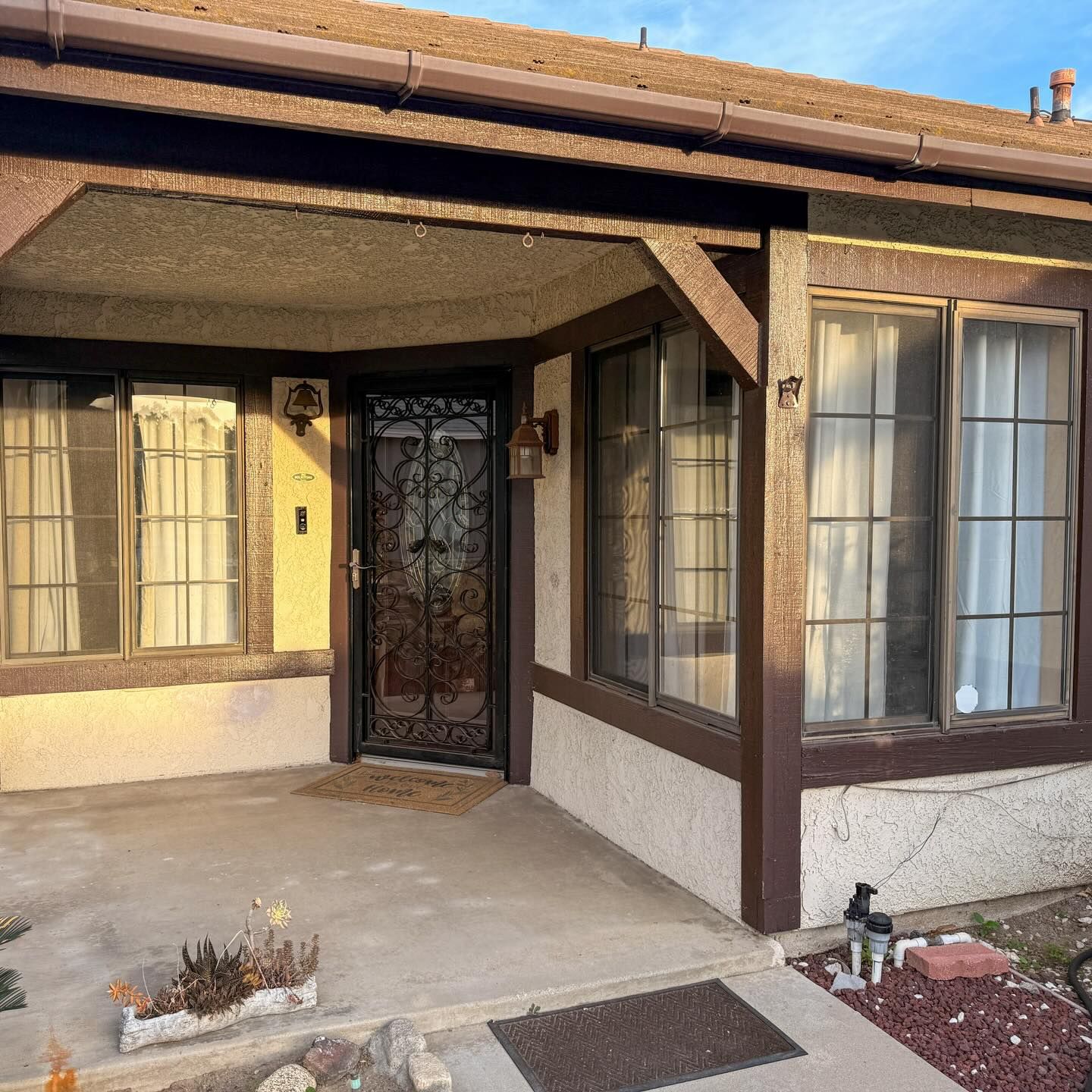 Front entrance of a house with brown trim, beige stucco, and a black iron security door.