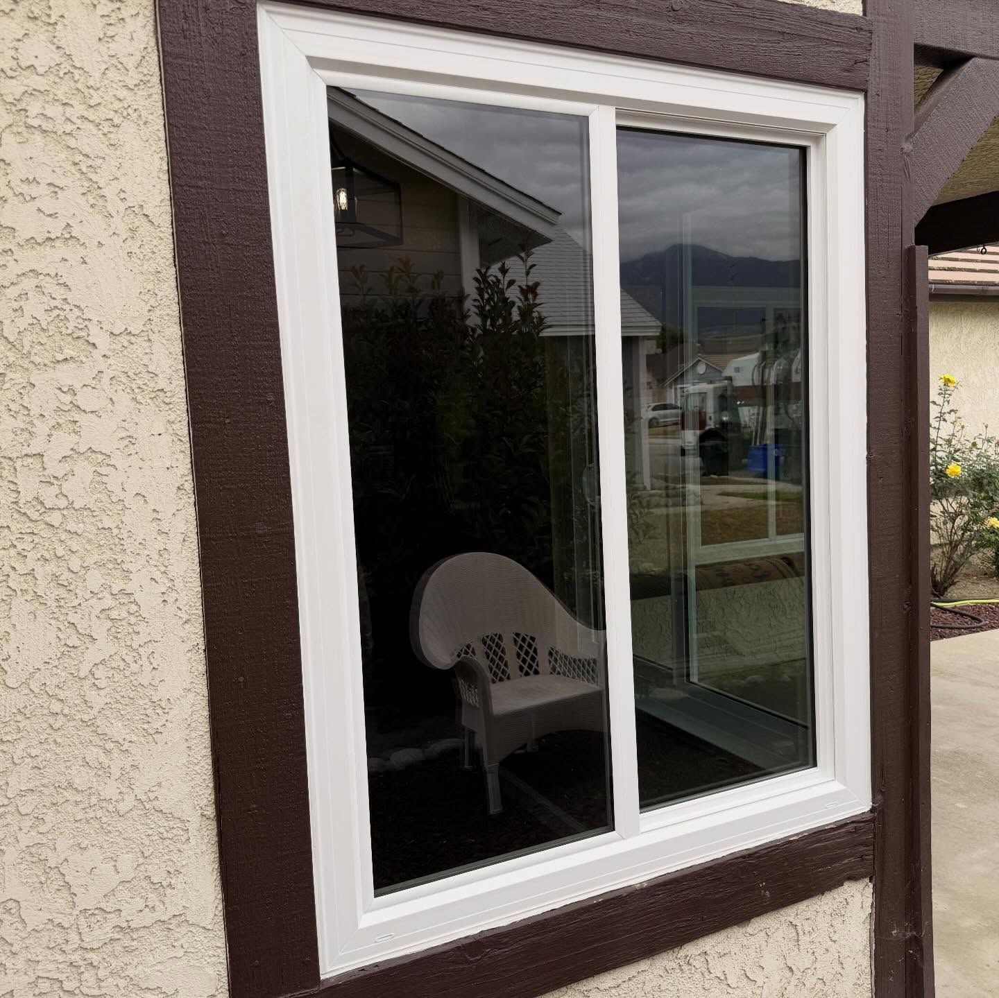 White-framed window in a beige stucco wall, reflecting a house and street outside.
