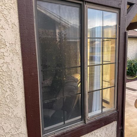 Brown-framed window with closed blinds and reflective glass on a stucco exterior wall