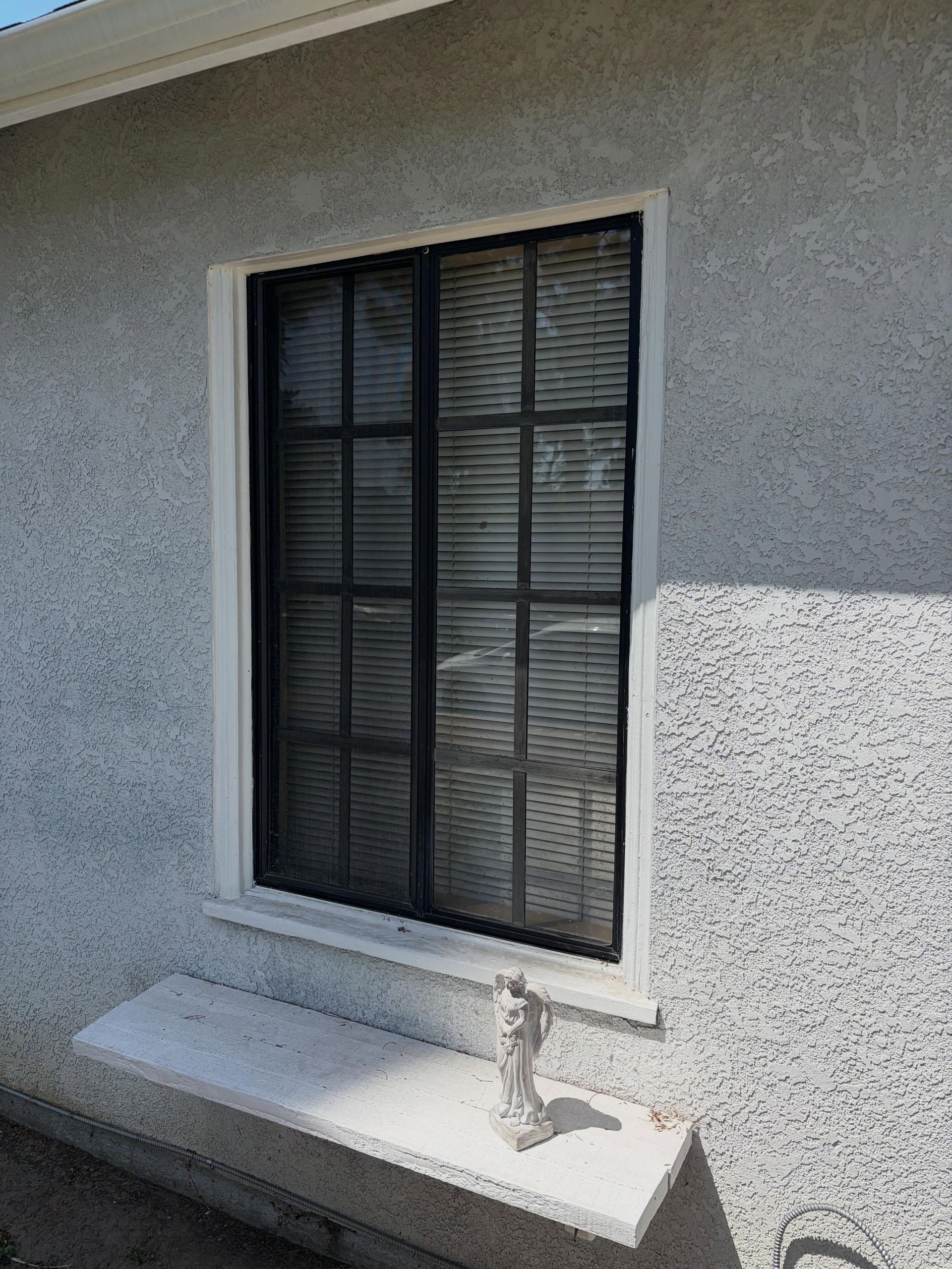 Black-framed window on a stucco exterior wall with a small cat figurine on the sill