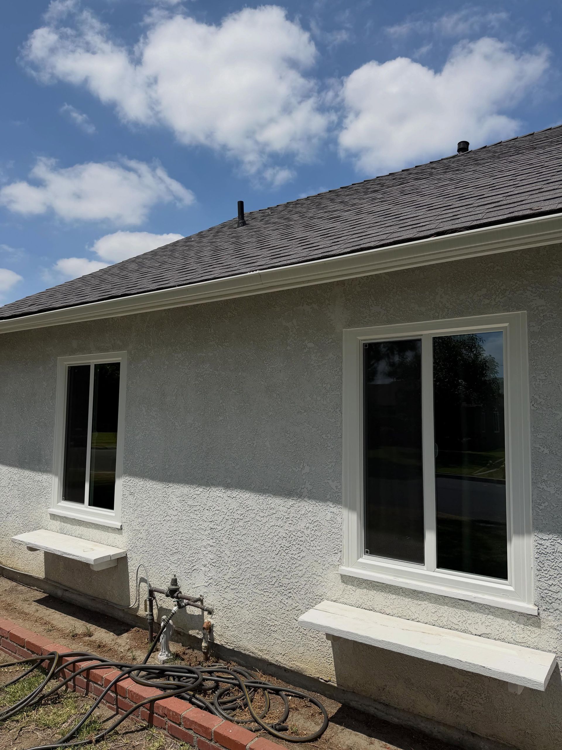 Exterior wall of a stucco house with two windows, flower boxes, and a cloudy blue sky.