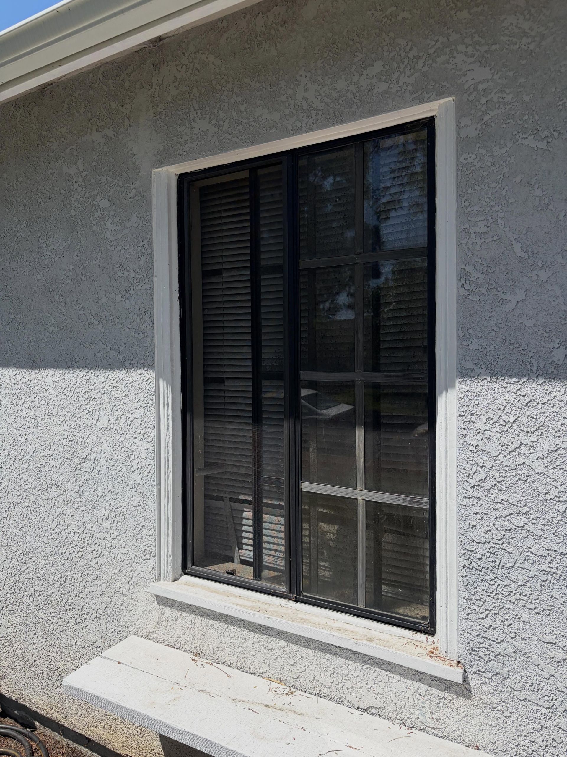 Exterior window with black shutters and a white sill on a textured gray wall