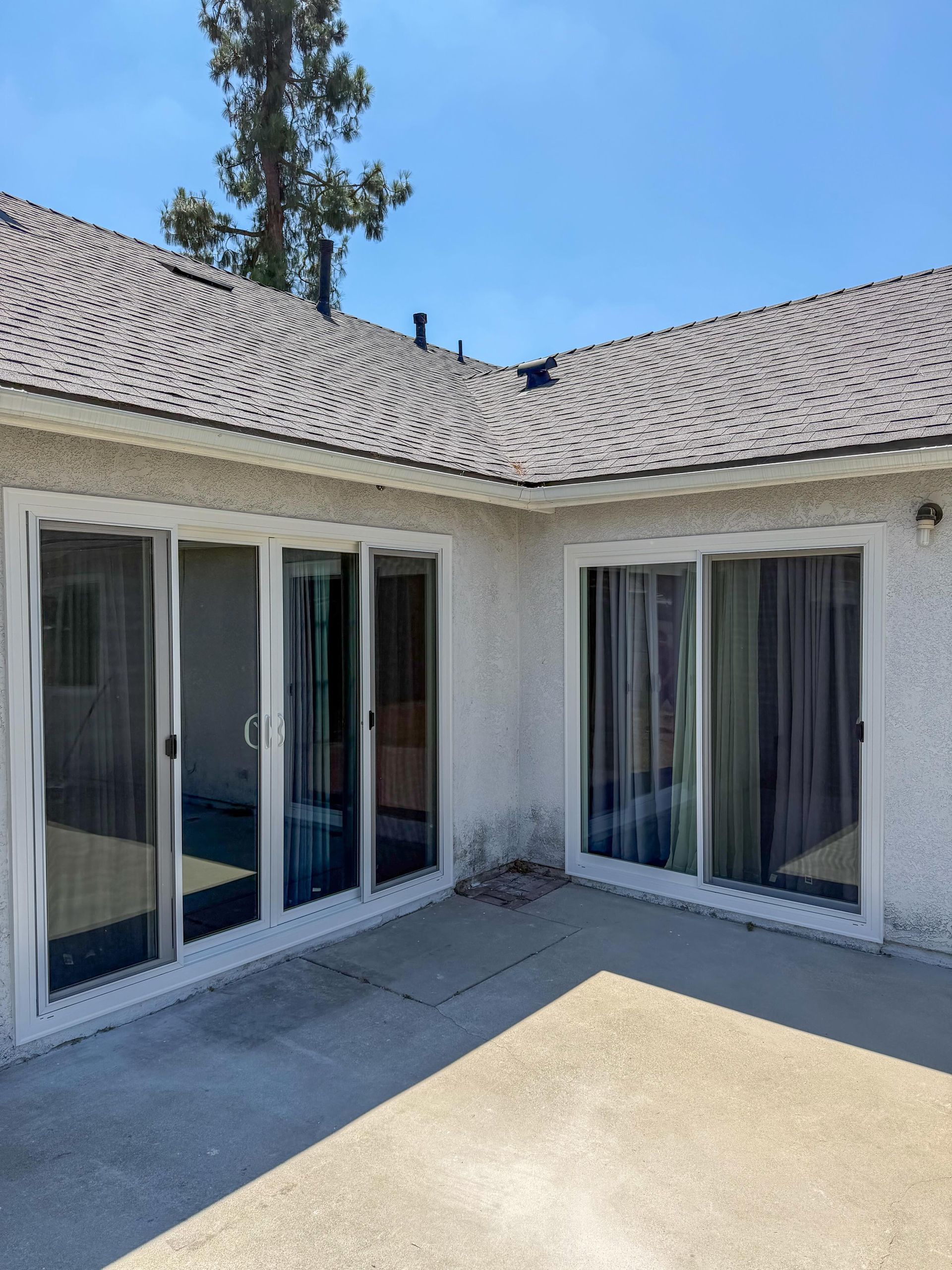 Patio with white sliding glass doors and windows under a tiled roof on a sunny day