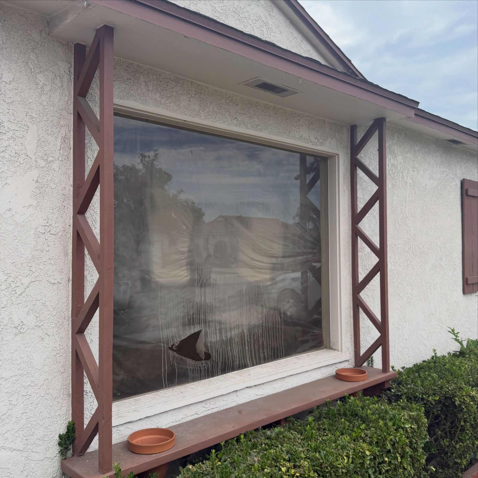 House window with sheer curtain, red wooden trim, and two small planters on the sill