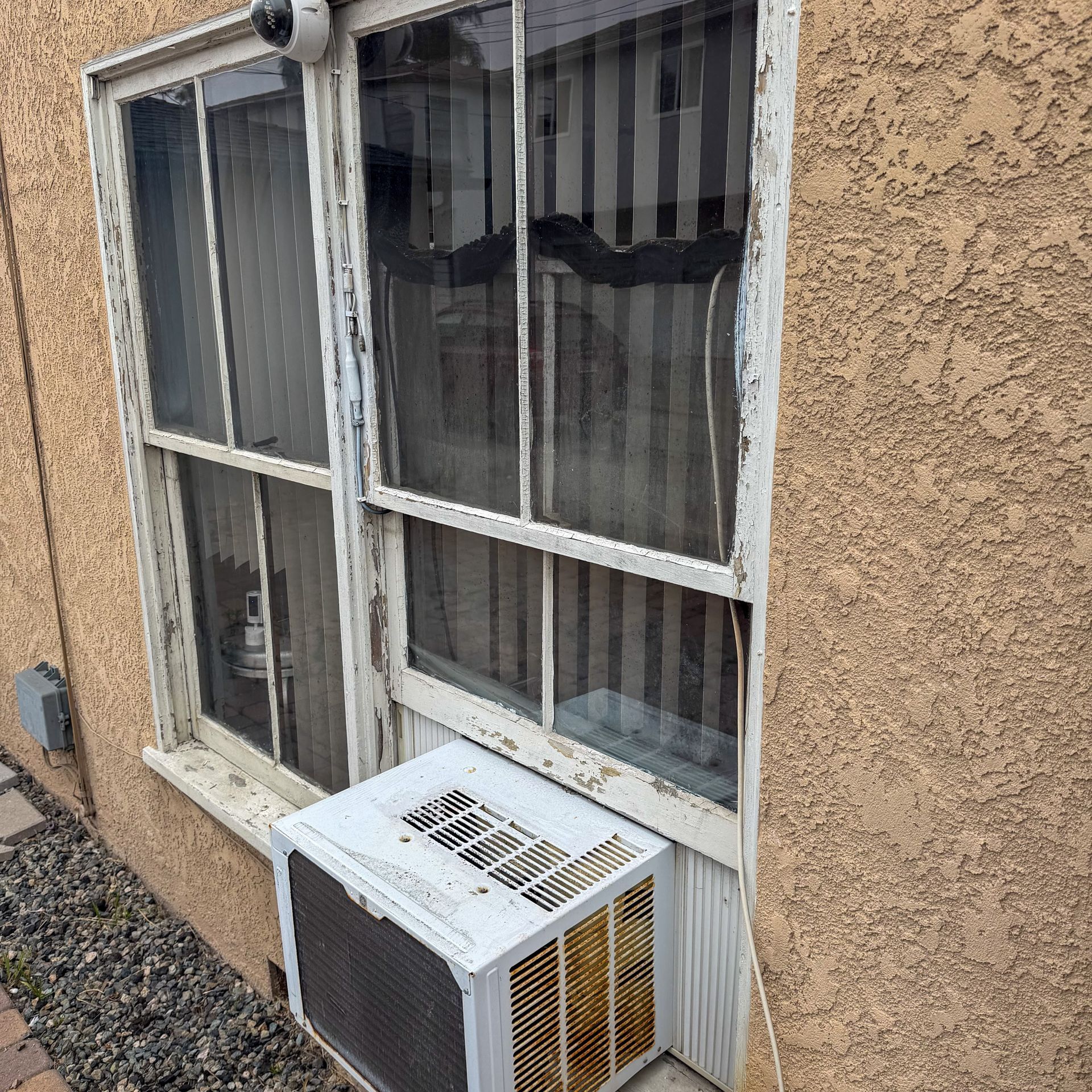 Window with striped curtains and a window air conditioner on a stucco exterior wall.
