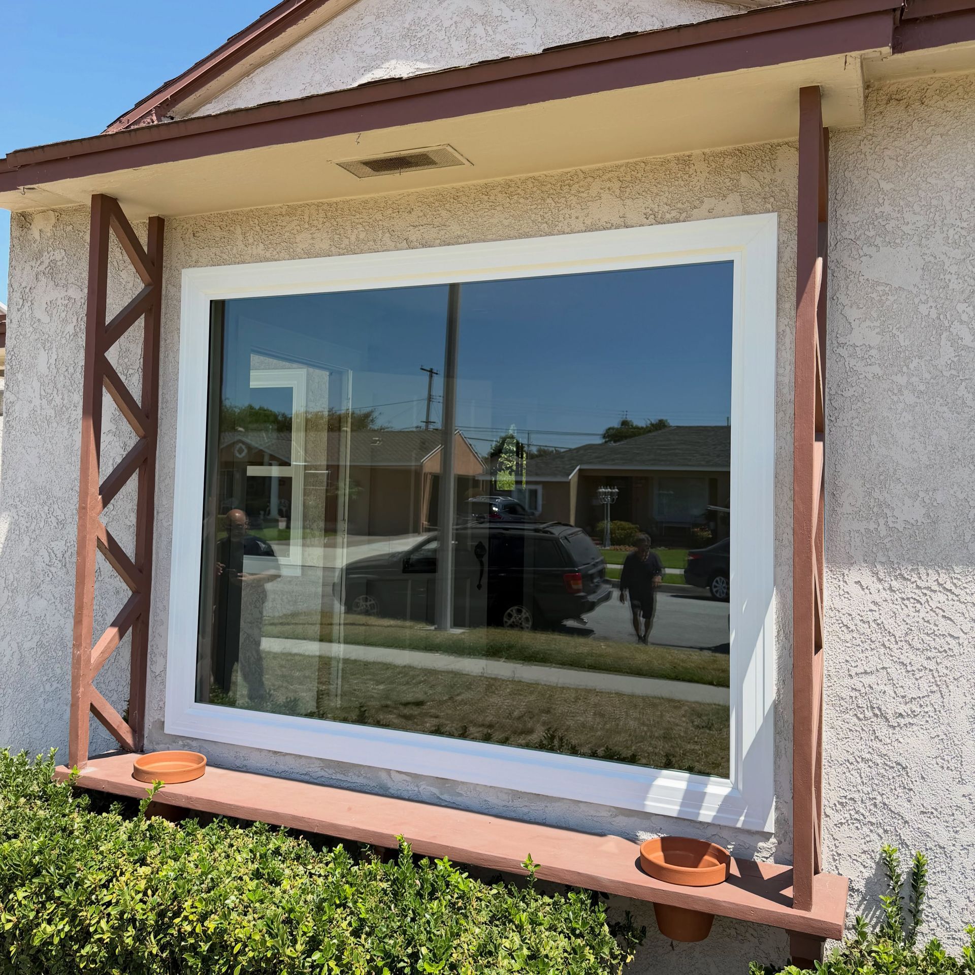 White-framed window in a stucco wall with brown decorative trim and reflected street scene.