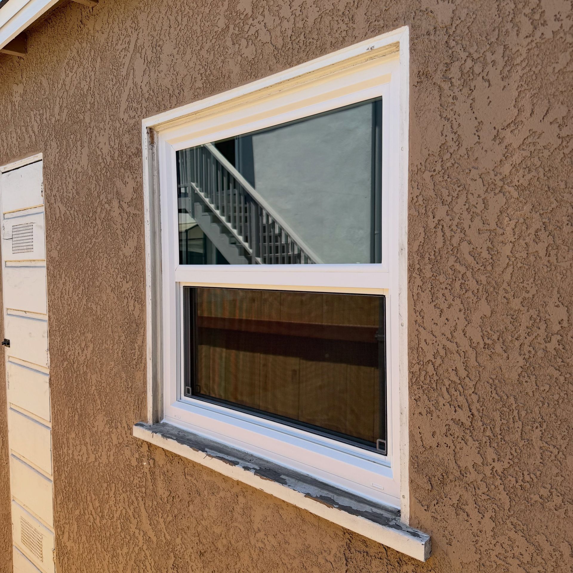 Close-up of a white-framed window with blinds set in a tan stucco wall.