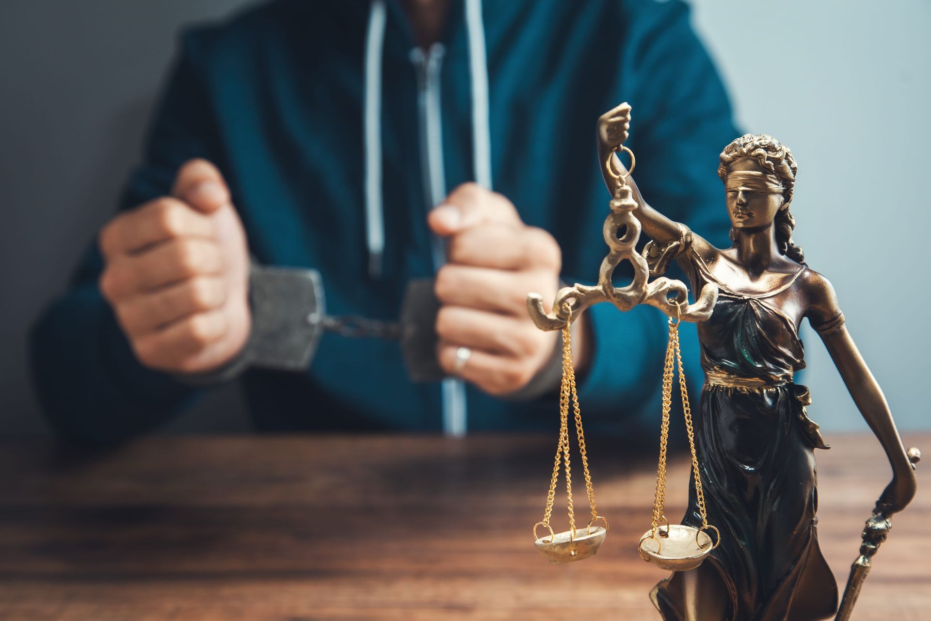 Bronze Lady Justice figurine in foreground, with blurred person holding handcuffs in the background