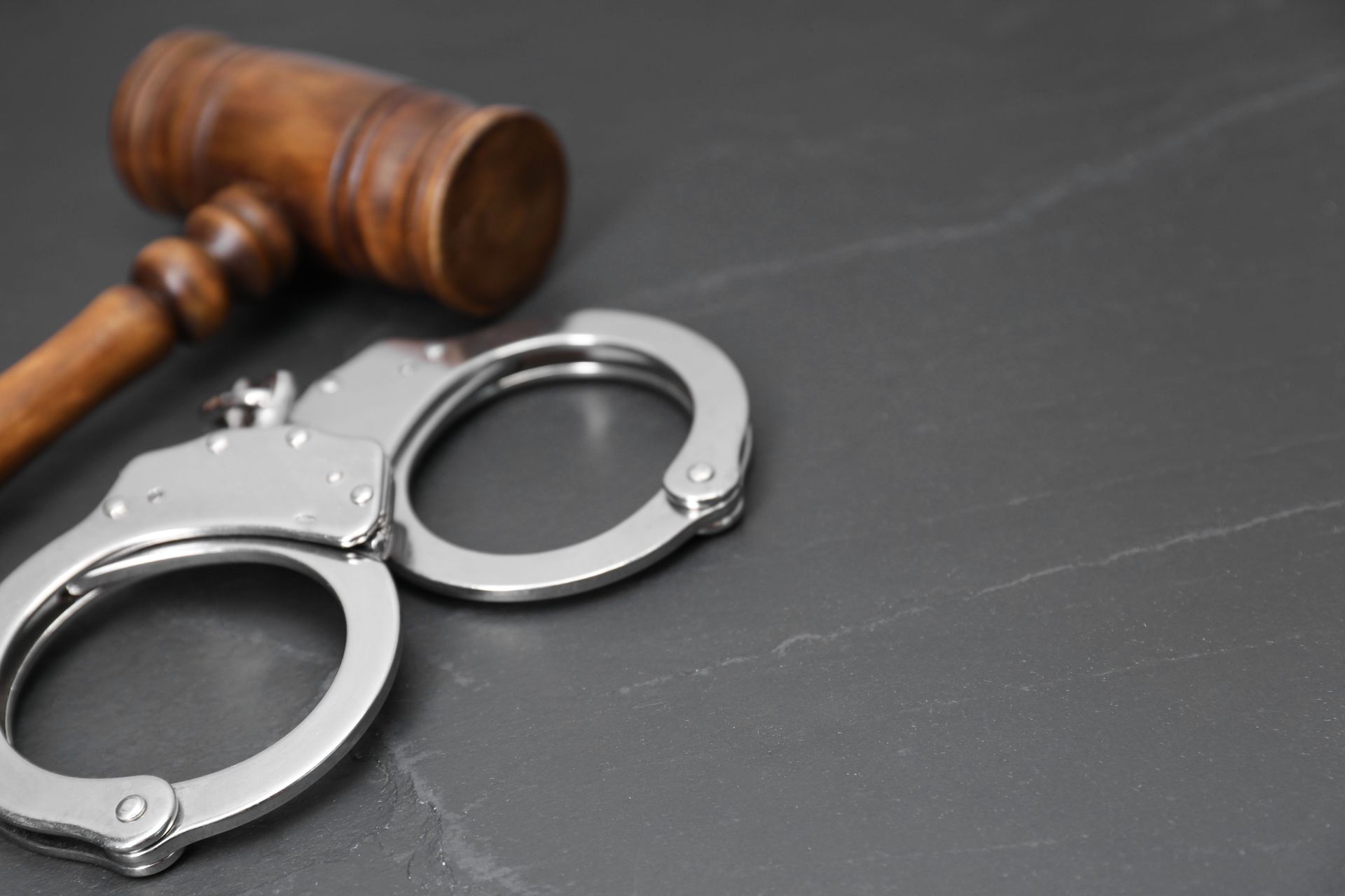 Silver handcuffs and wooden gavel on a dark gray surface.