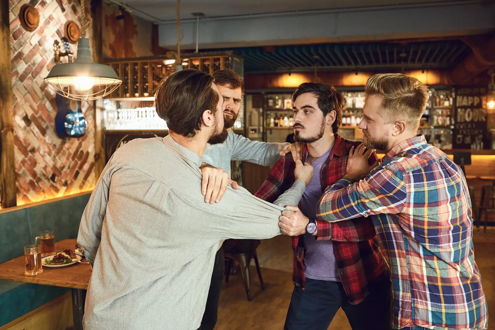 Three men in plaid shirts greet each other with a friendly group embrace in a cozy bar.