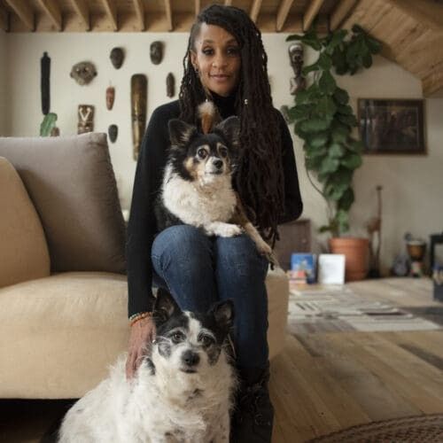 Woman seated indoors with two small dogs in a cozy living room