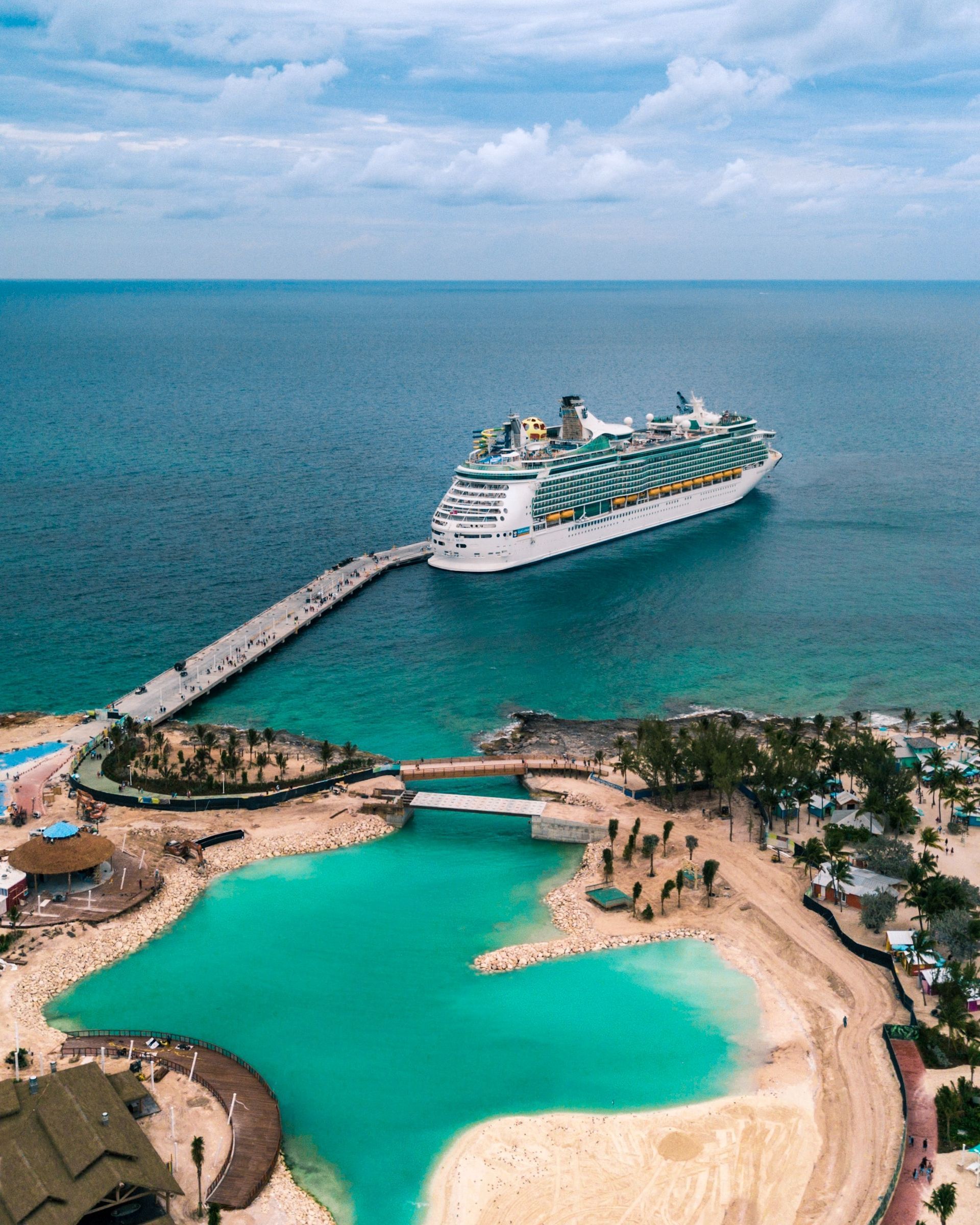 Cruise ship docked at a tropical island with turquoise water and sandy beaches.