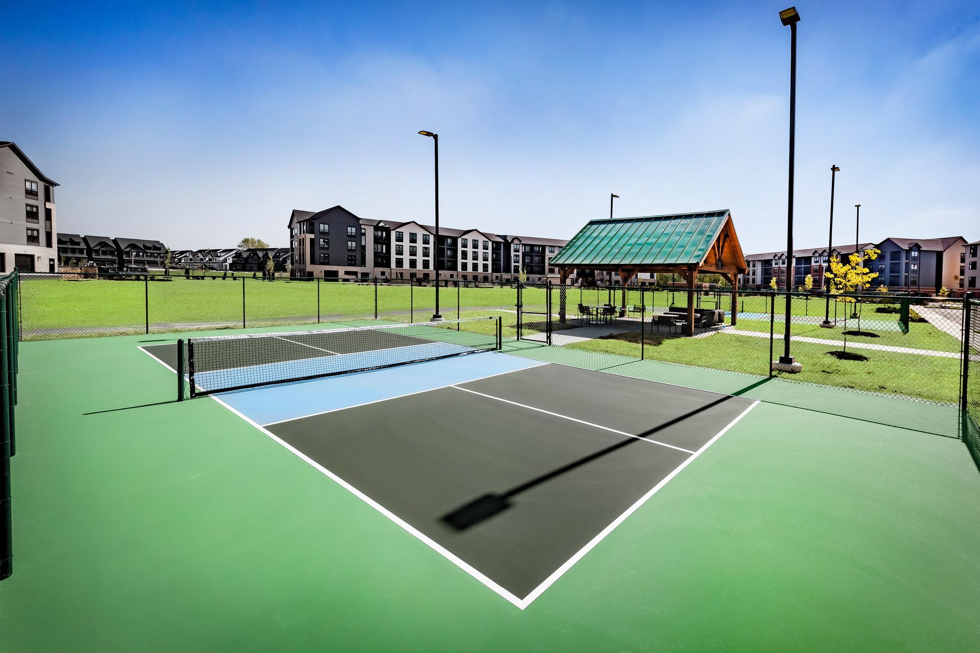 Pickleball court with net. Green and blue court, buildings in the background, sunny day at River Place Flats in Fishers, IN.