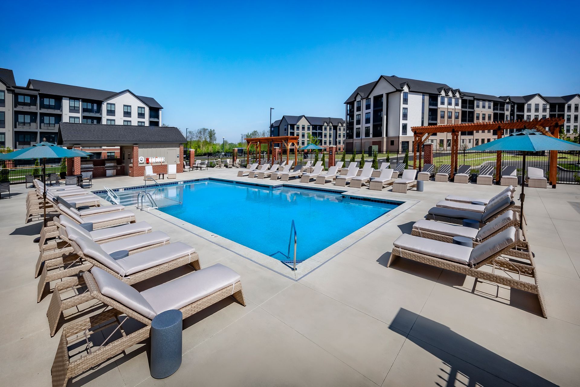 Pool with lounge chairs, umbrellas, and apartment buildings in the background on a sunny day at River Place Flats in Fishers, IN.