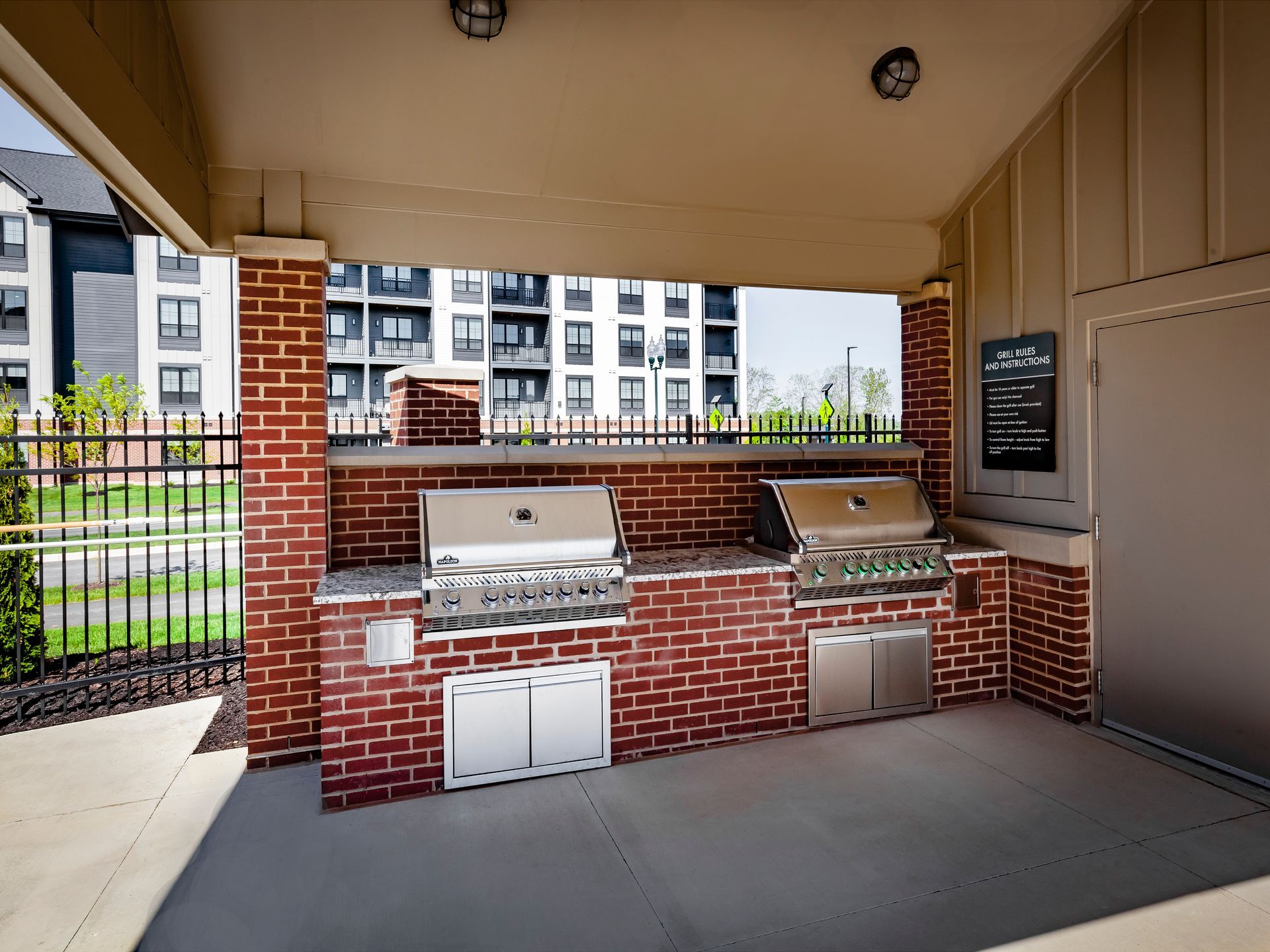Outdoor brick grilling station with two grills, stainless steel doors, and black sign at River Place Flats in Fishers, IN.