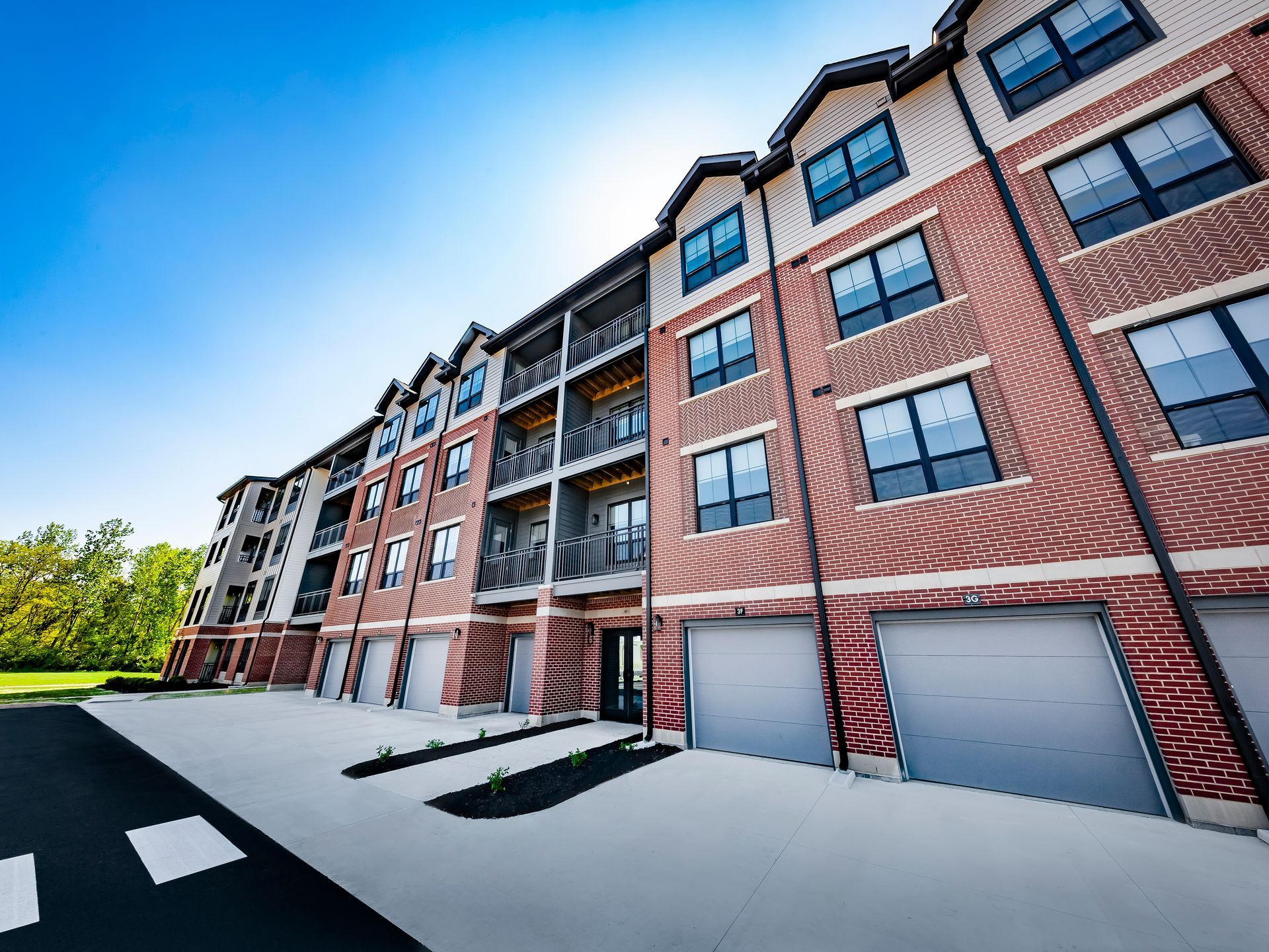 Brick apartment building with attached garages, under a blue sky at River Place Flats in Fishers, IN.